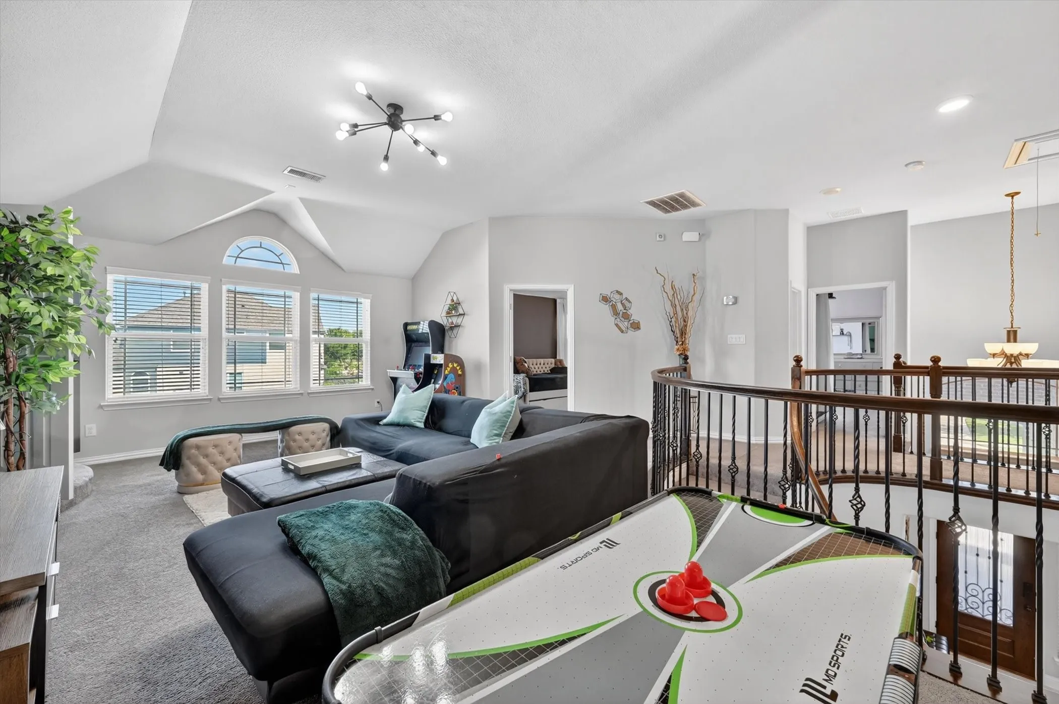 Carpeted loft area featuring a vaulted ceiling with a modern light fixture, three windows with blinds, and an arched transom window