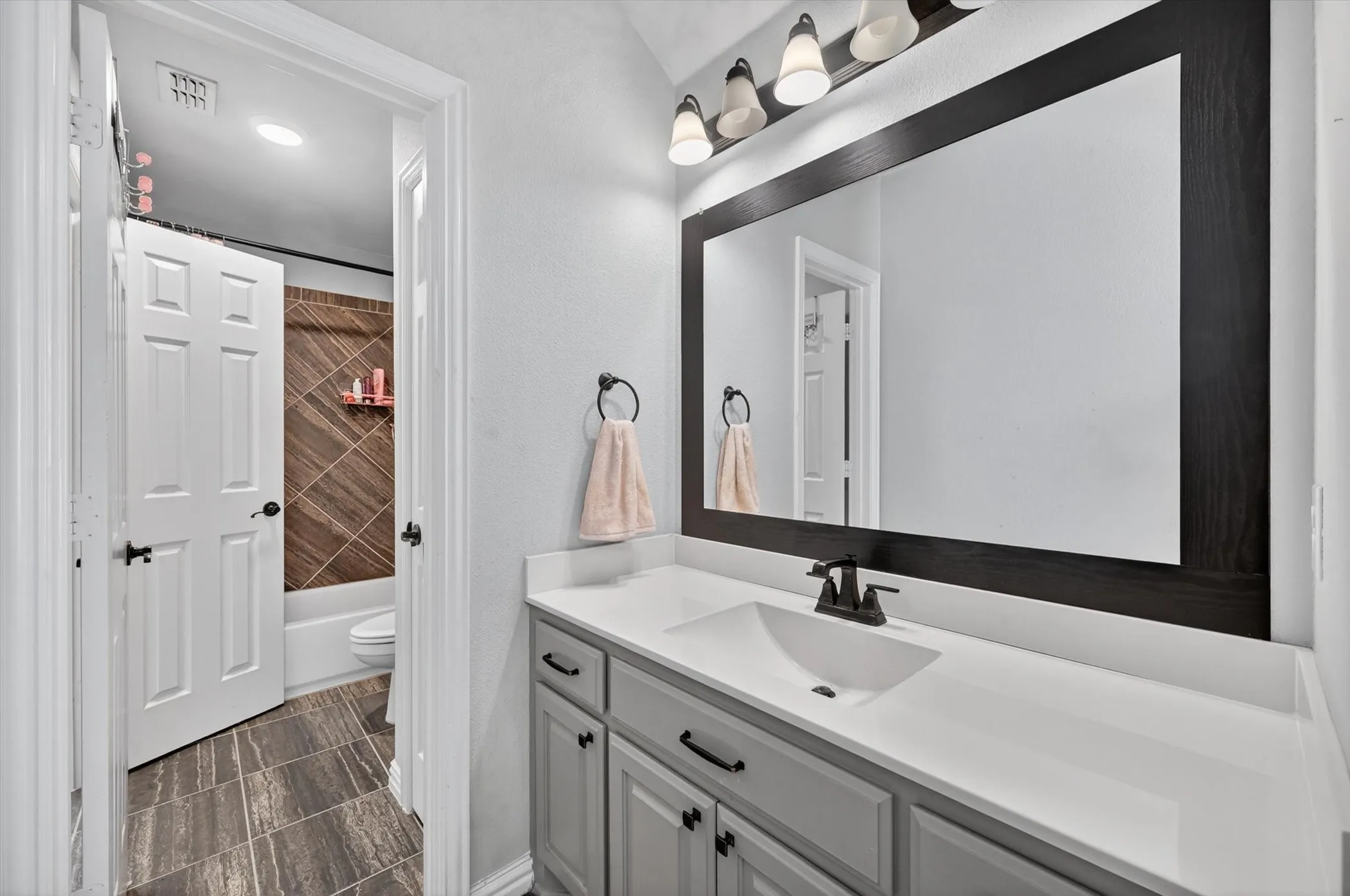 Vanity area featuring a framed mirror with integrated lighting, a white countertop, and gray cabinetry with dark hardware