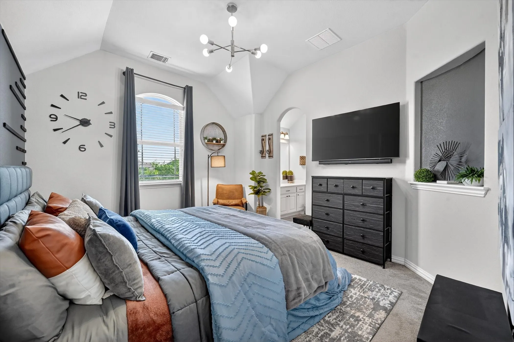Vaulted ceiling bedroom featuring a large arched window with blinds, recessed architectural alcoves, and light gray carpet flooring