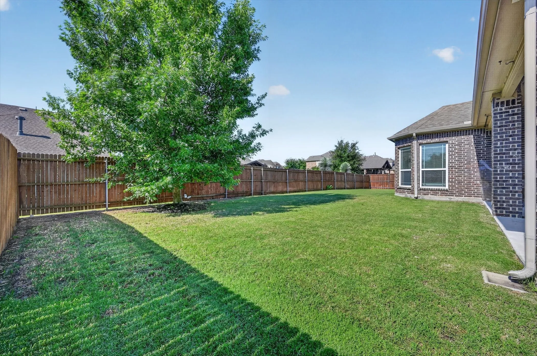 Expansive rear lawn featuring a mature tree, privacy fencing, and a brick exterior with multiple windows