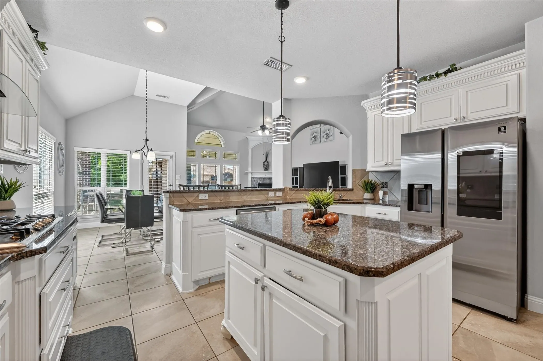 Spacious kitchen featuring an island with a stone countertop, white cabinetry with crown molding, stainless steel appliances, and tile flooring