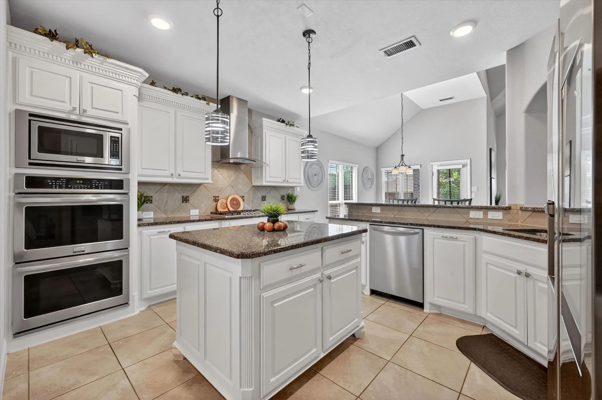 Kitchen featuring white cabinetry, granite countertops, tile flooring, stainless steel appliances, and a central island