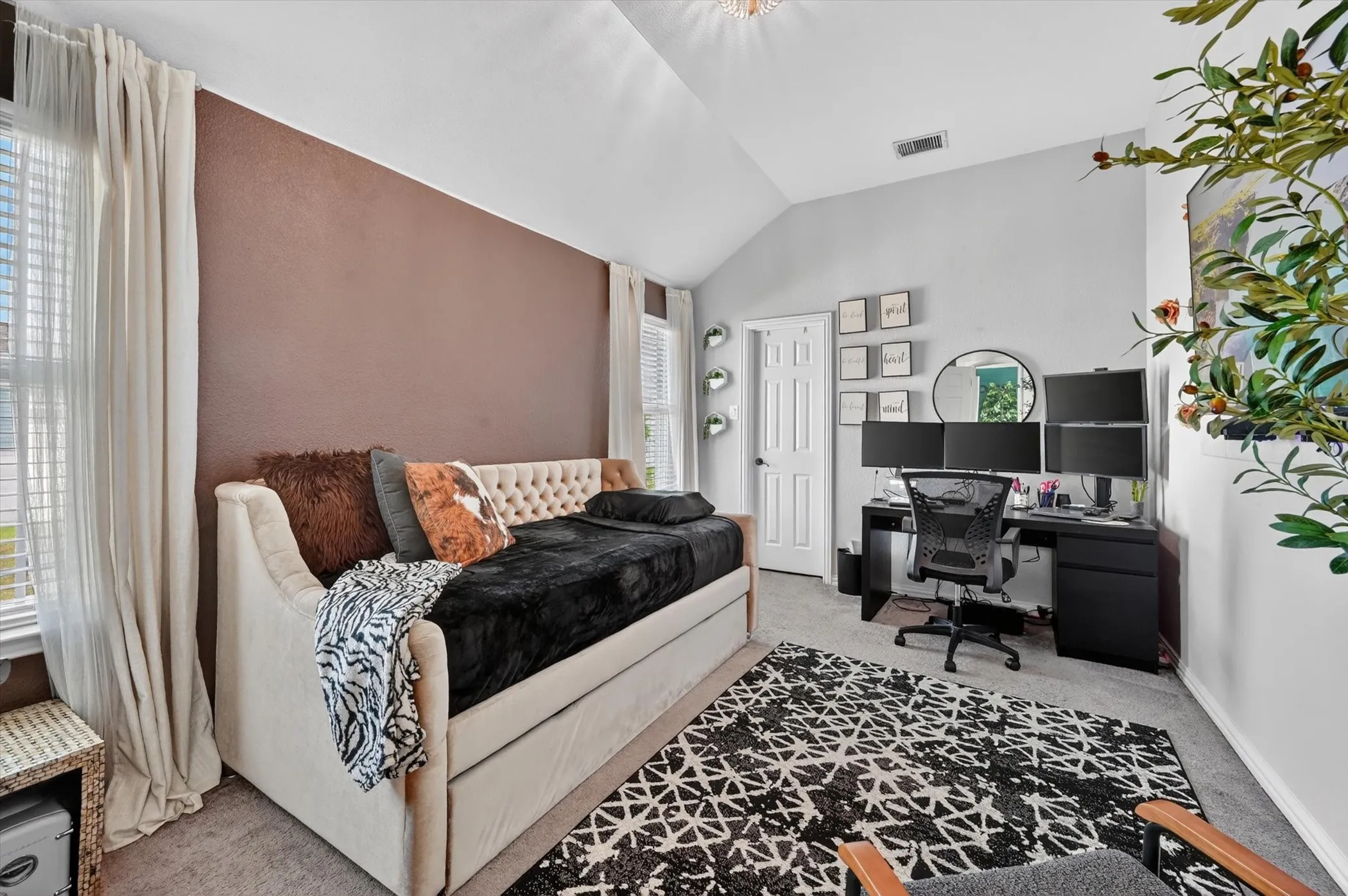 Vaulted ceiling room featuring a dedicated workspace with built-in desk, plush carpeting, window treatments, and a contrasting accent wall