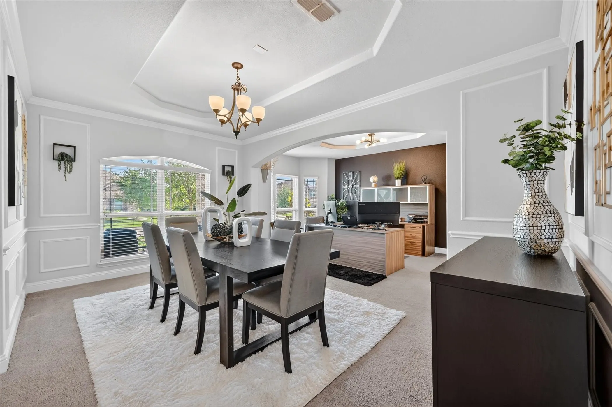 Dining area featuring a tray ceiling with a chandelier, decorative wall molding, arched entryways, and a large window with horizontal blinds
