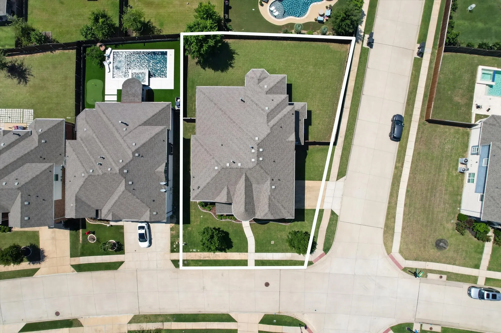 Expansive corner lot featuring a sizable lawn, concrete driveway, and established landscaping