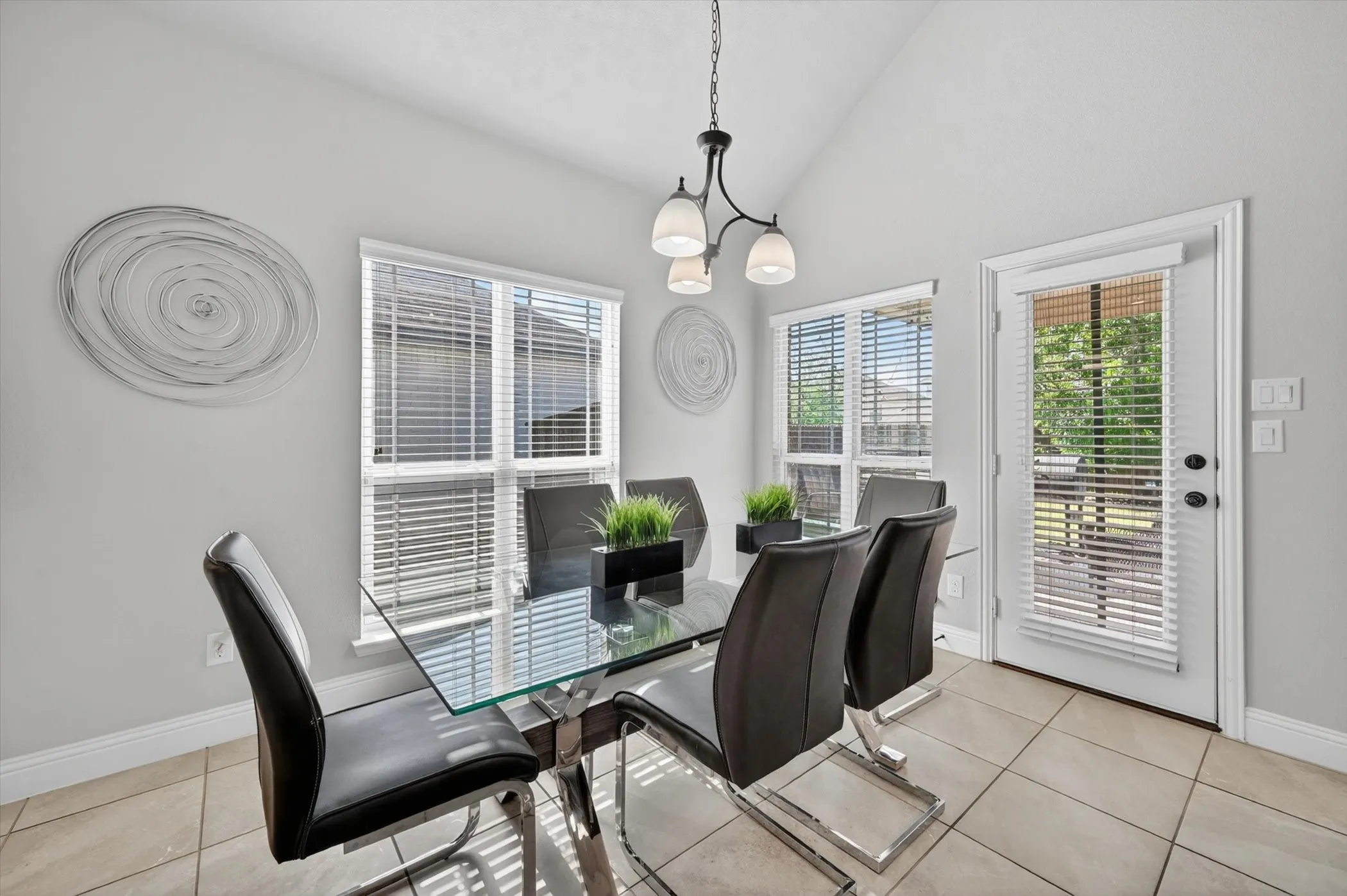 Vaulted ceiling dining area featuring tile flooring, a multi-pane window with horizontal blinds, and a white door with horizontal blinds