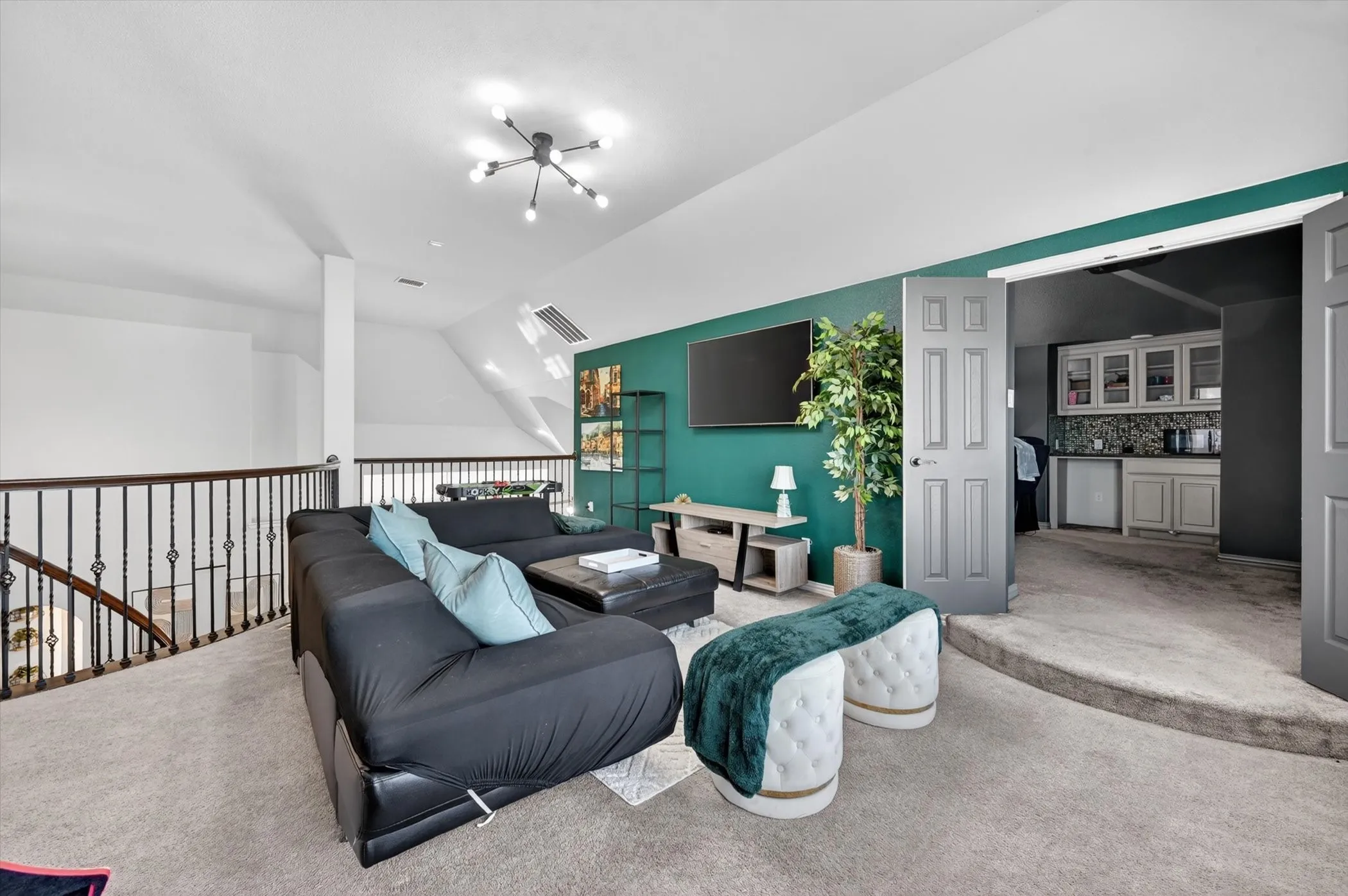 Carpeted loft area featuring a striking accent wall, a distinctive modern sputnik chandelier, and an open stairwell with wrought iron balusters