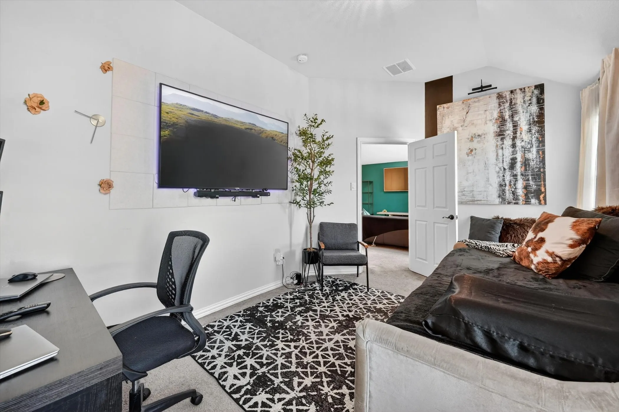 Carpeted interior space featuring a mounted television display, a dark wood-finish desk, and a decorative area rug