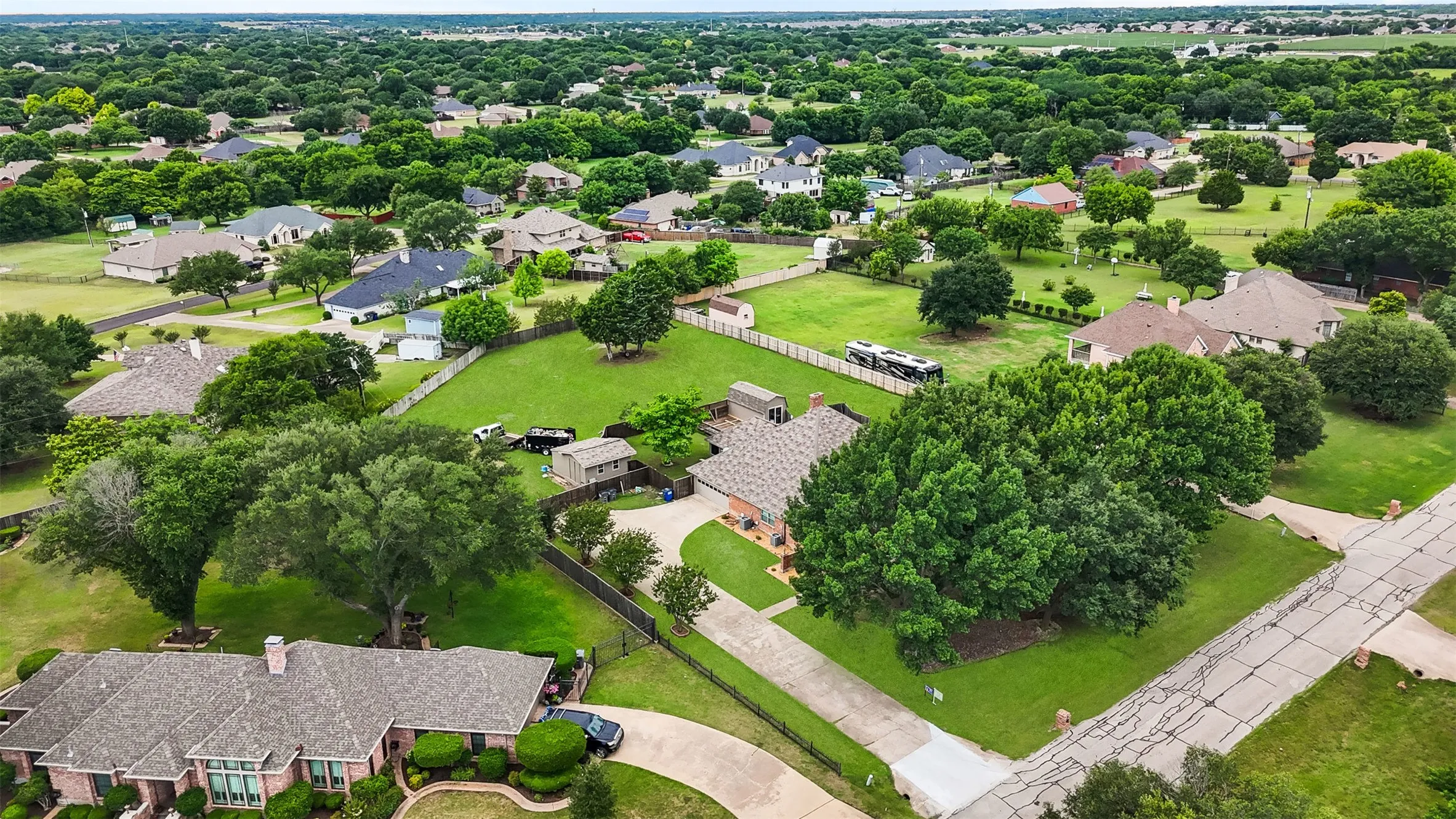 Expansive property featuring a sizable green lawn, mature trees, and a paved driveway