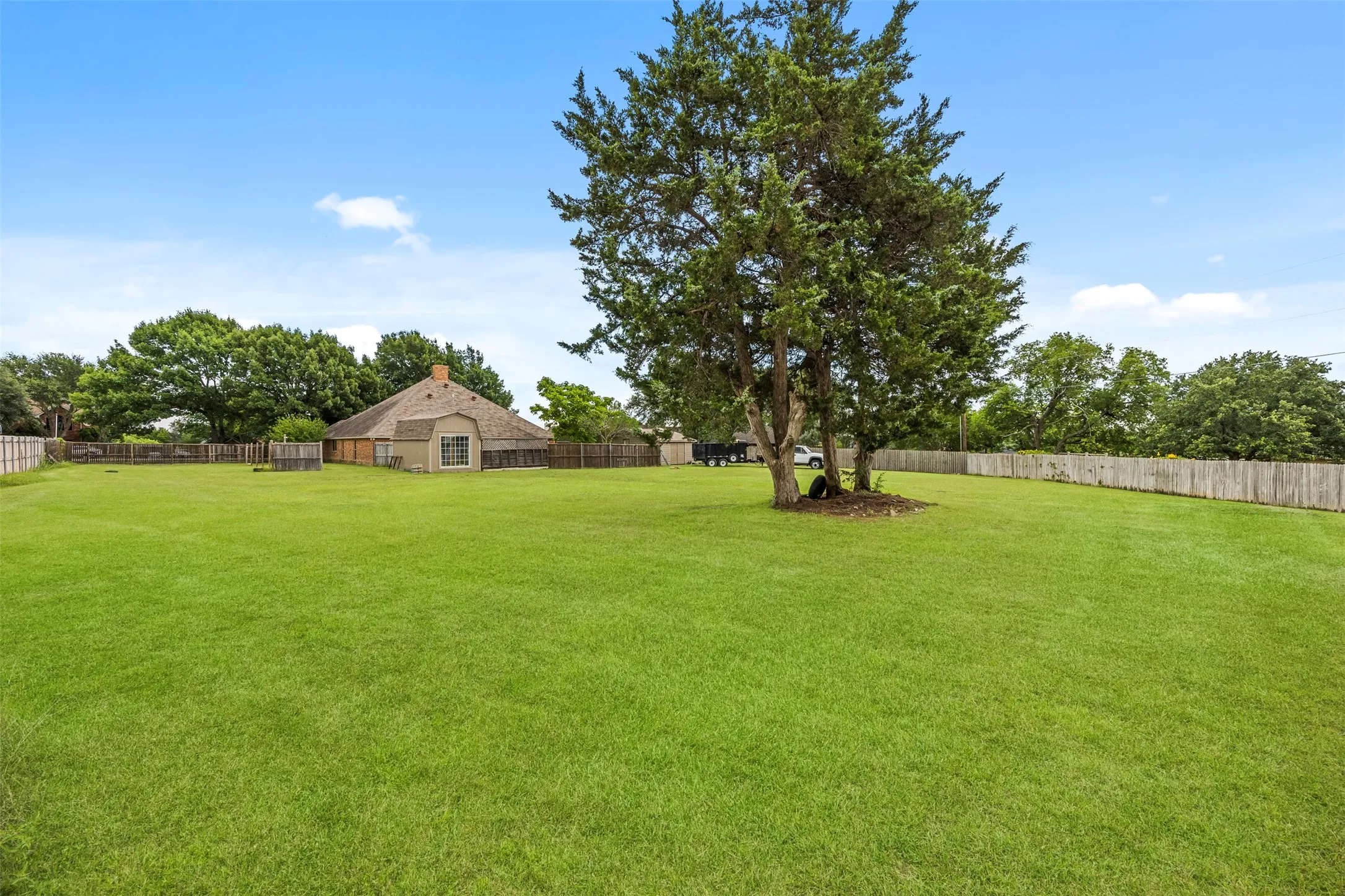 Expansive green lawn with mature trees and a perimeter wood fence