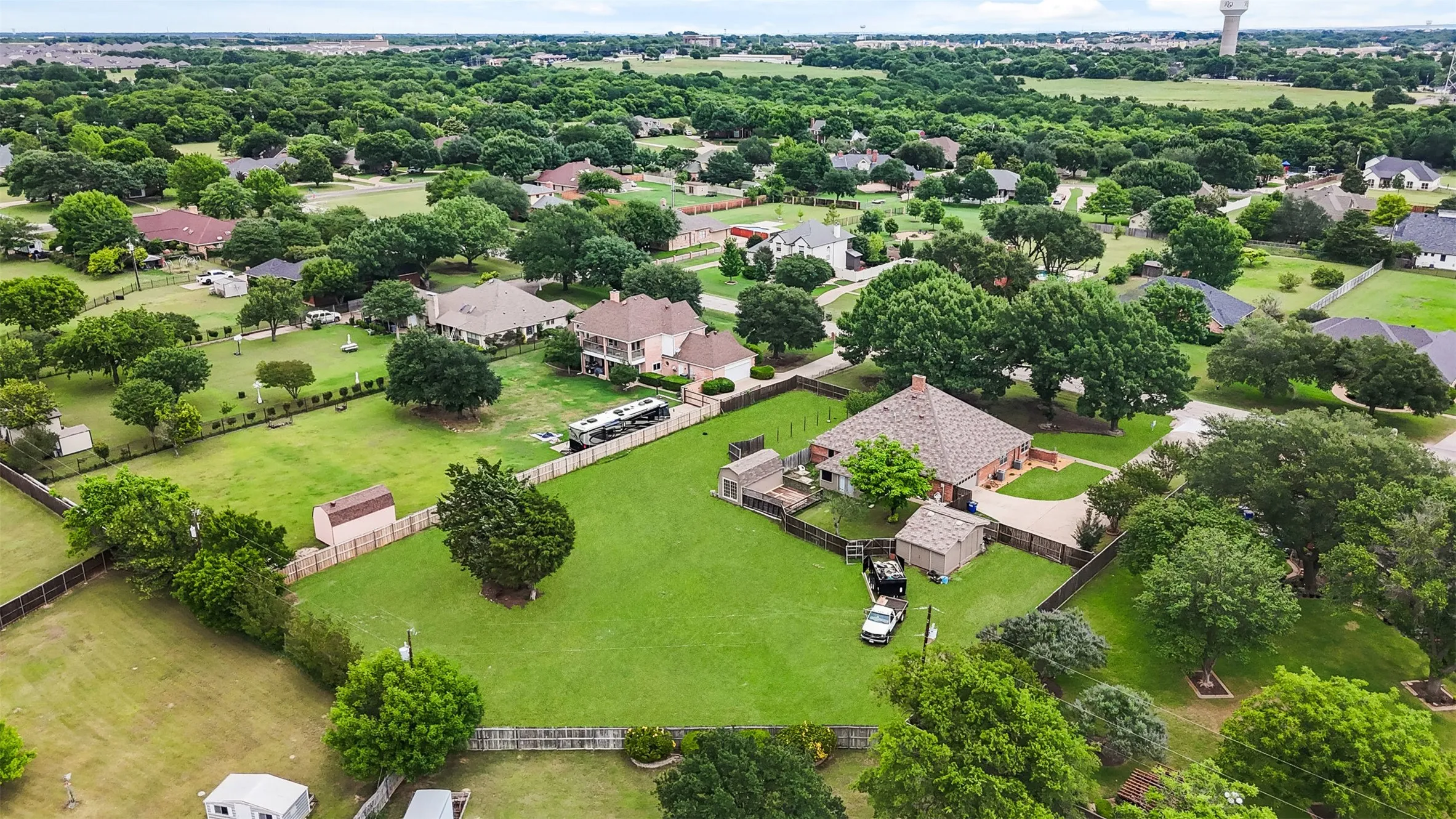 Expansive residential property featuring a large green lawn, mature trees, and a brick-built home with a gabled roof