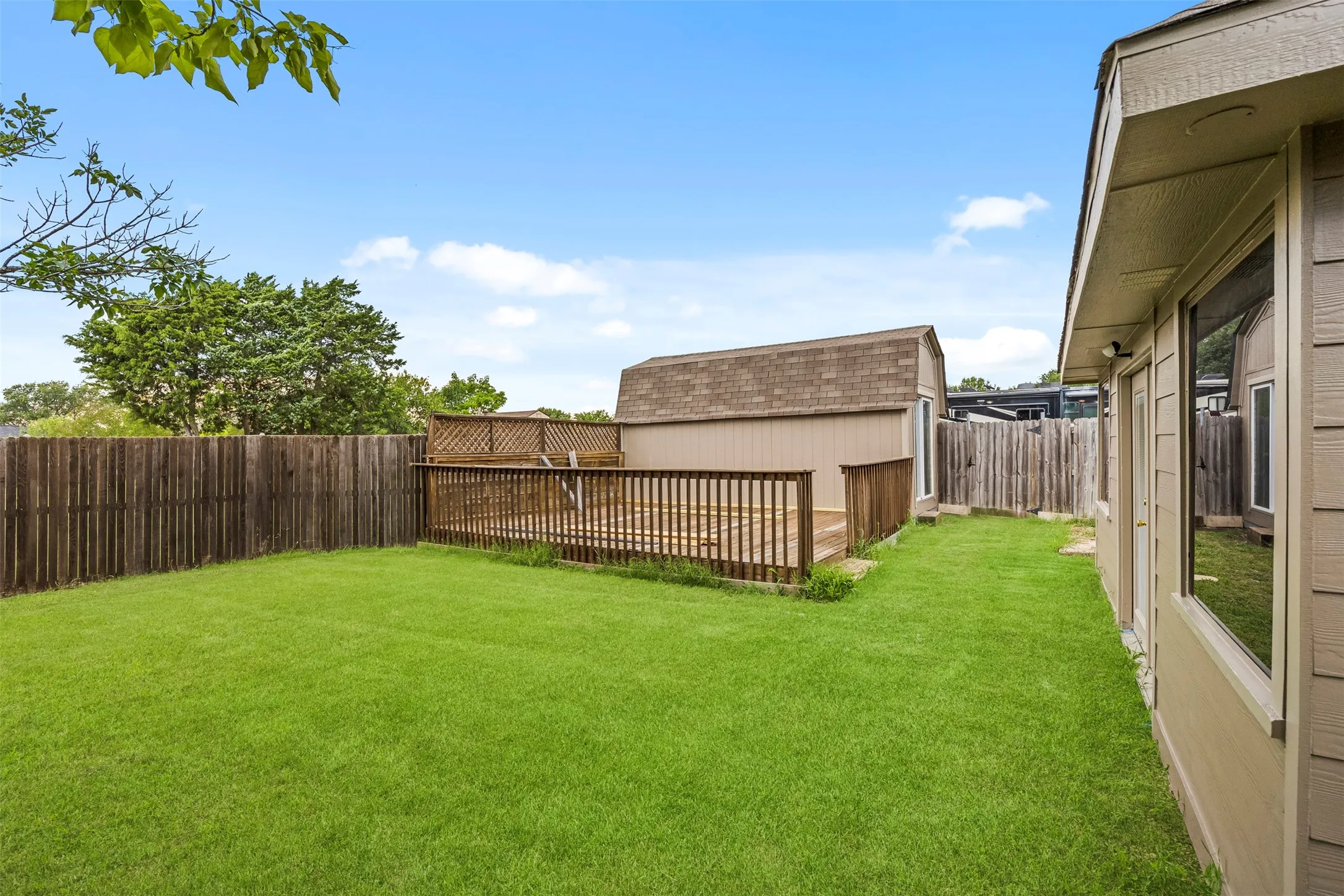 Expansive backyard featuring a lush lawn, privacy fencing, and a raised wood deck
