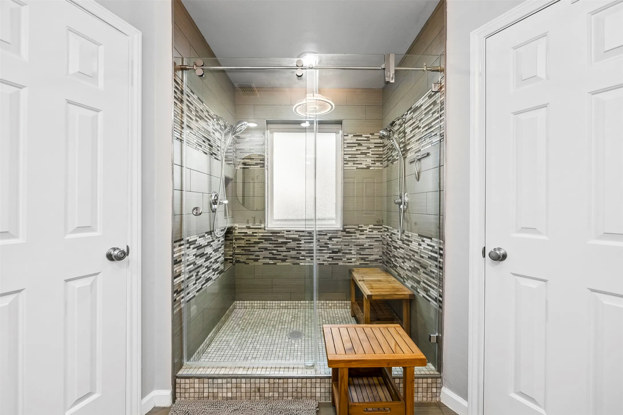 Glass-enclosed shower featuring a rain shower head, mosaic tile accents, and a frosted window