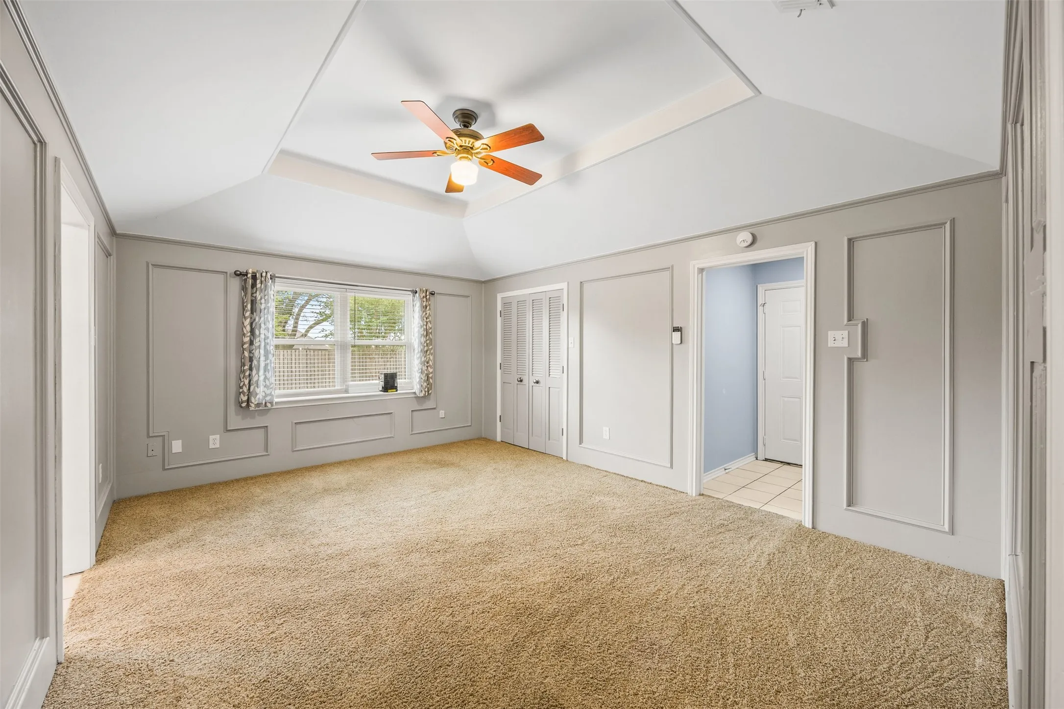 Room featuring a vaulted ceiling with a ceiling fan, wall trim details, and carpet flooring