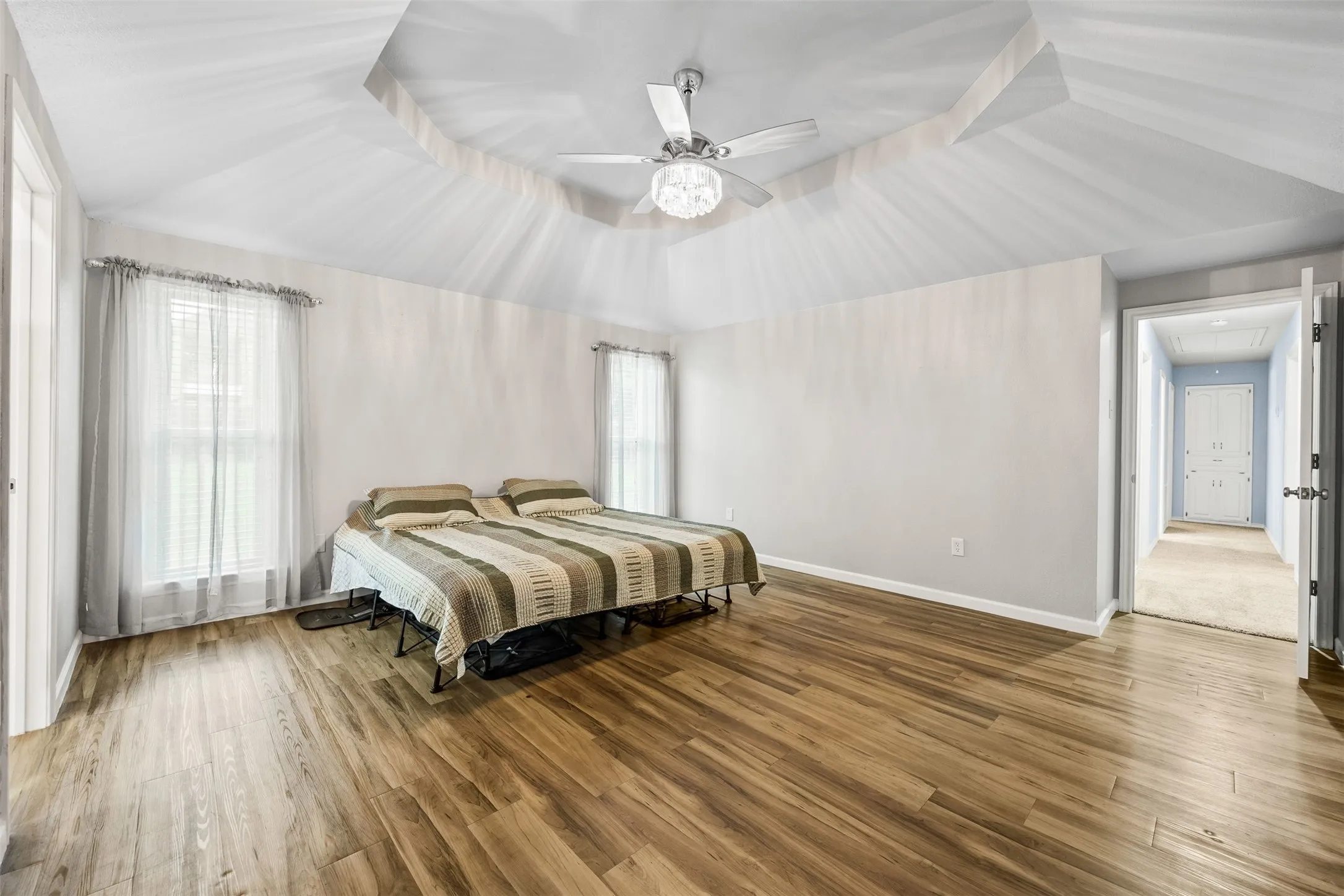Spacious room featuring wood-finish flooring, a tray ceiling, and a ceiling fan with integrated lighting