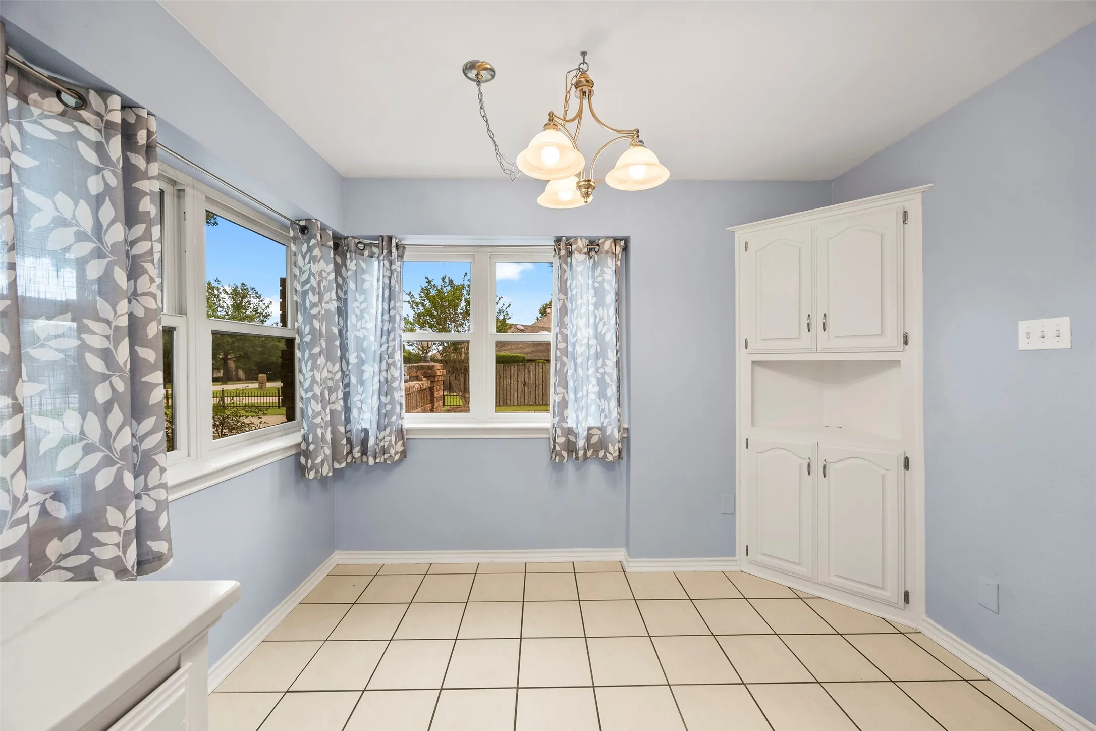 Light-toned tile flooring complements the built-in corner cabinetry, featuring both enclosed and open shelving