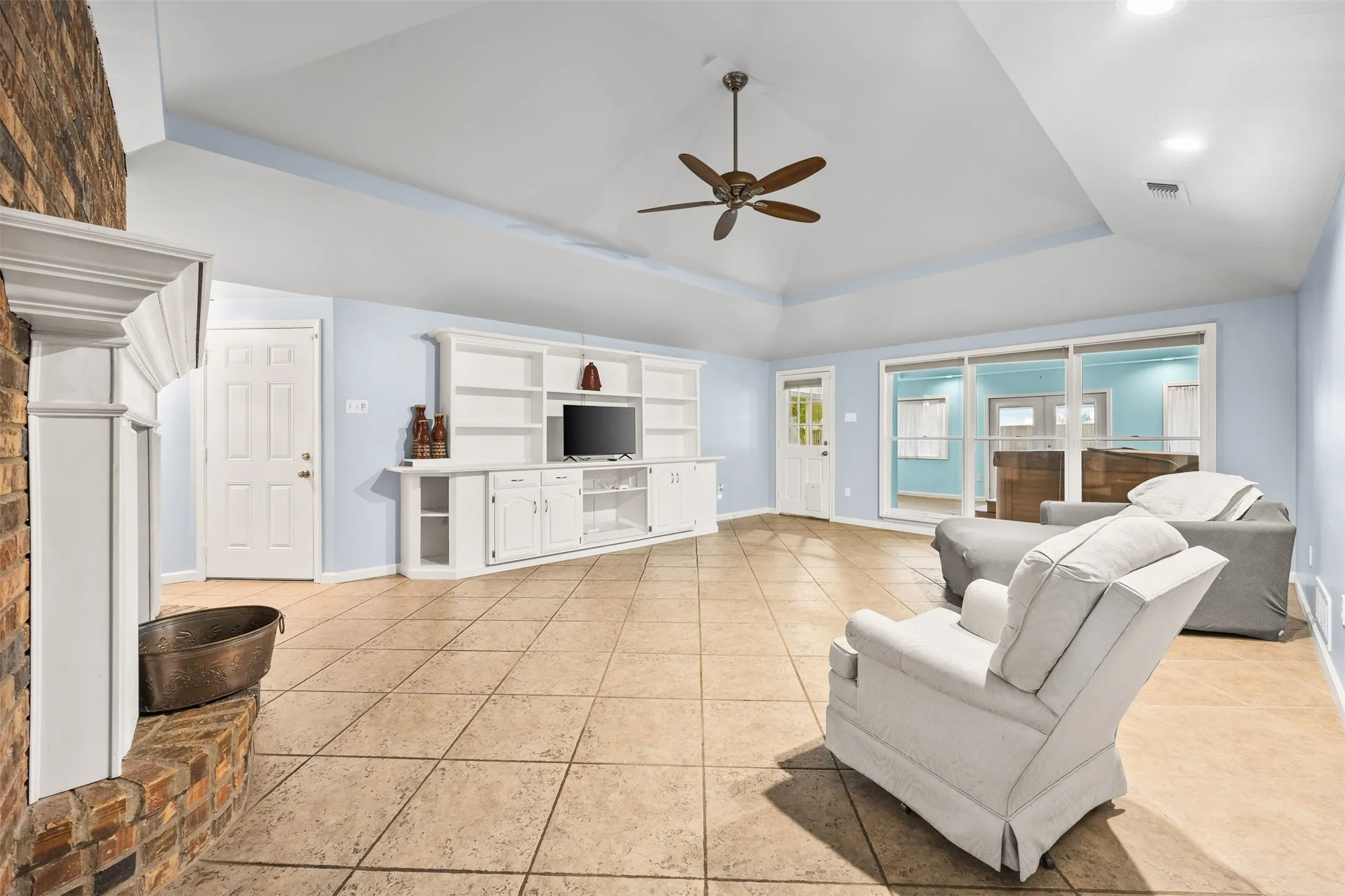 Spacious interior featuring a brick fireplace with a white mantel, an integrated entertainment center with shelving and cabinetry, and large format tile flooring