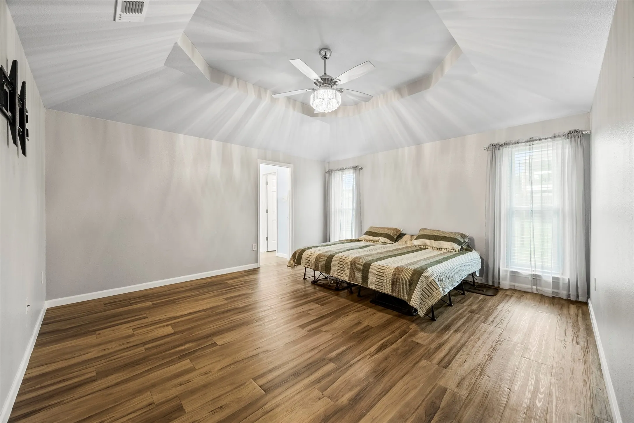 Interior room featuring wood-finish flooring, a tray ceiling with a central fan light fixture, and two window openings with sheer curtains