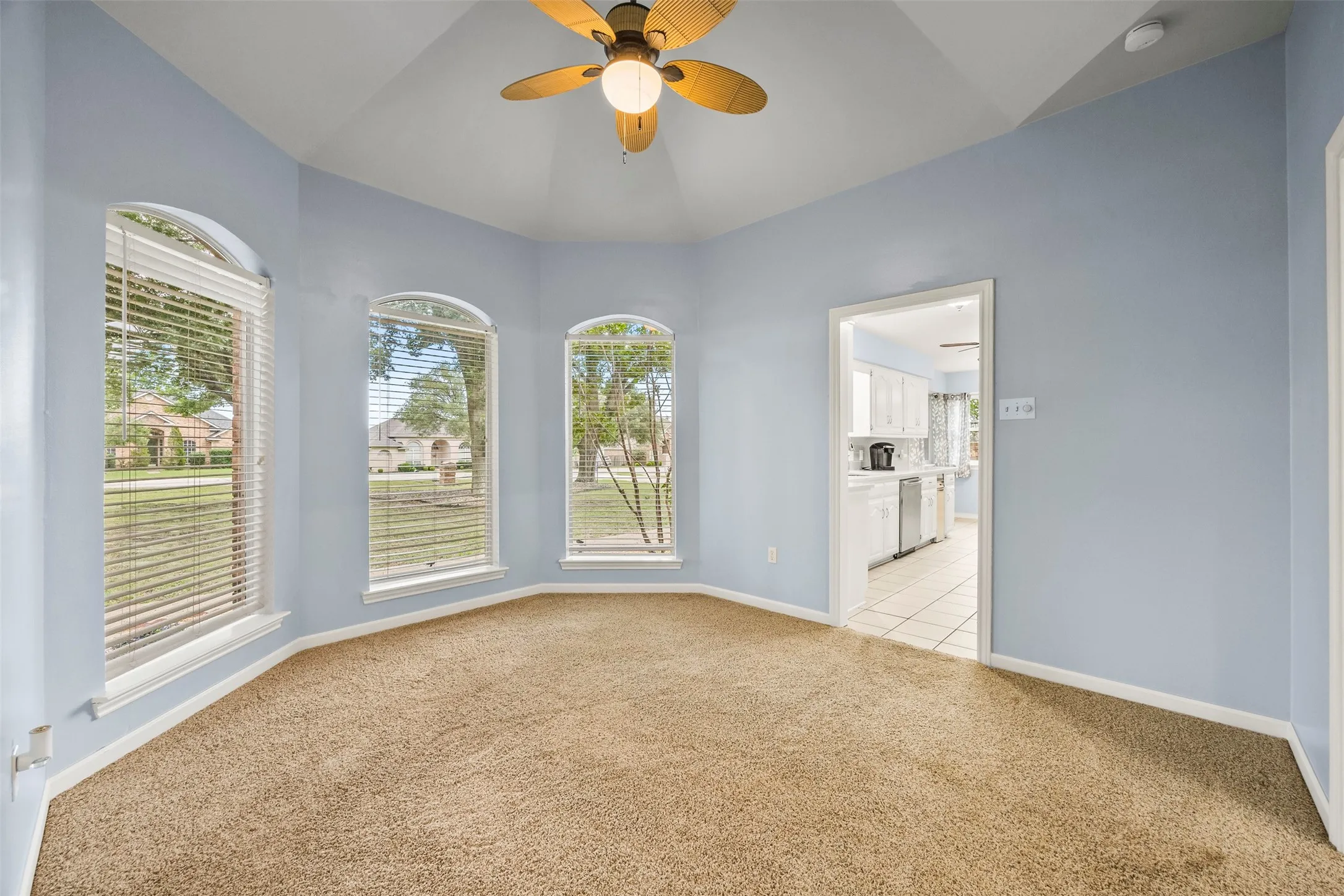Bay window area featuring arched windows with blinds, a ceiling fan, light blue wall paint, and brown carpet flooring