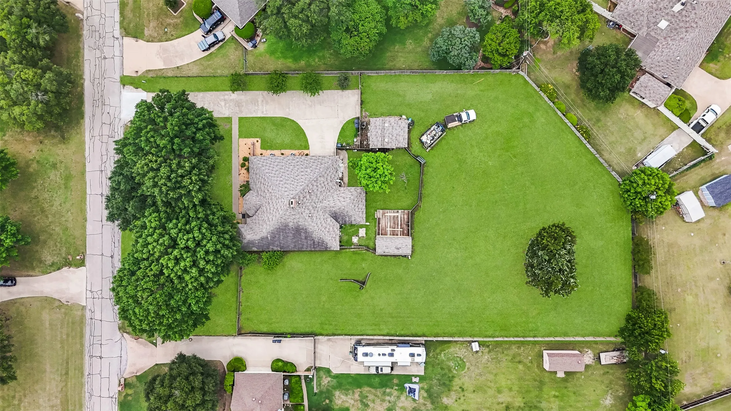 Expansive property featuring a large residence with a shingle roof, a spacious green lawn, mature trees, and a concrete driveway