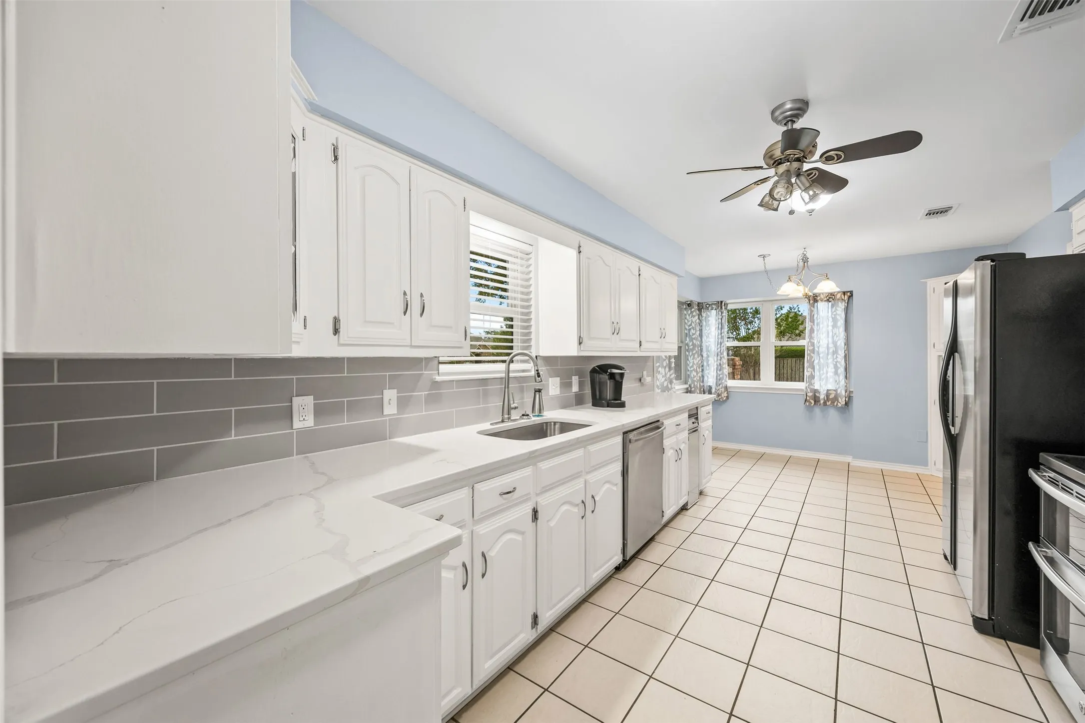 Kitchen featuring light-toned cabinetry, light-toned countertops, a gray subway tile backsplash, and stainless steel appliances