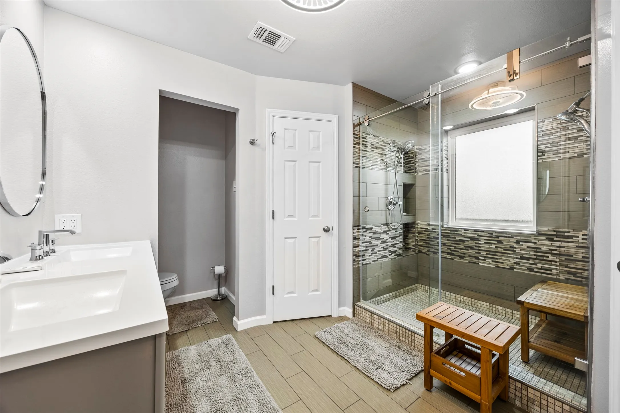 Contemporary bathroom featuring a double vanity with integrated sinks, a glass-enclosed shower with subway tile, a decorative mosaic tile accent band, and a separate water closet