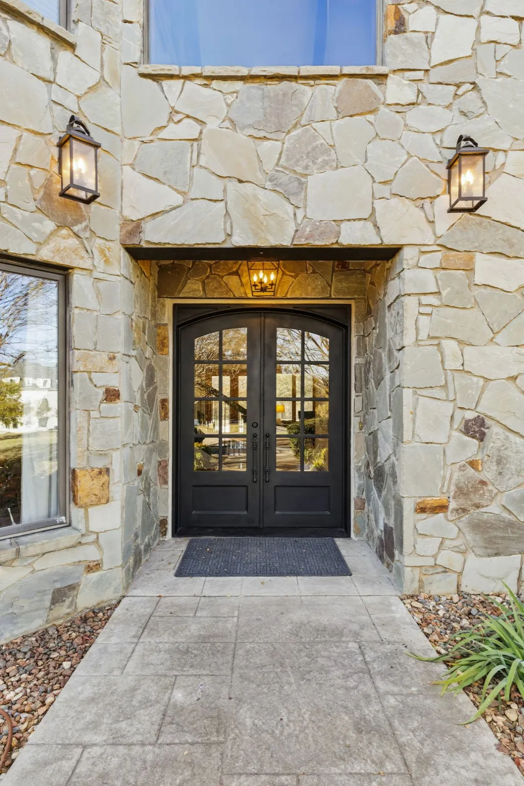 Stone facade entry with double arched glass-panel doors, complemented by two exterior wall lanterns