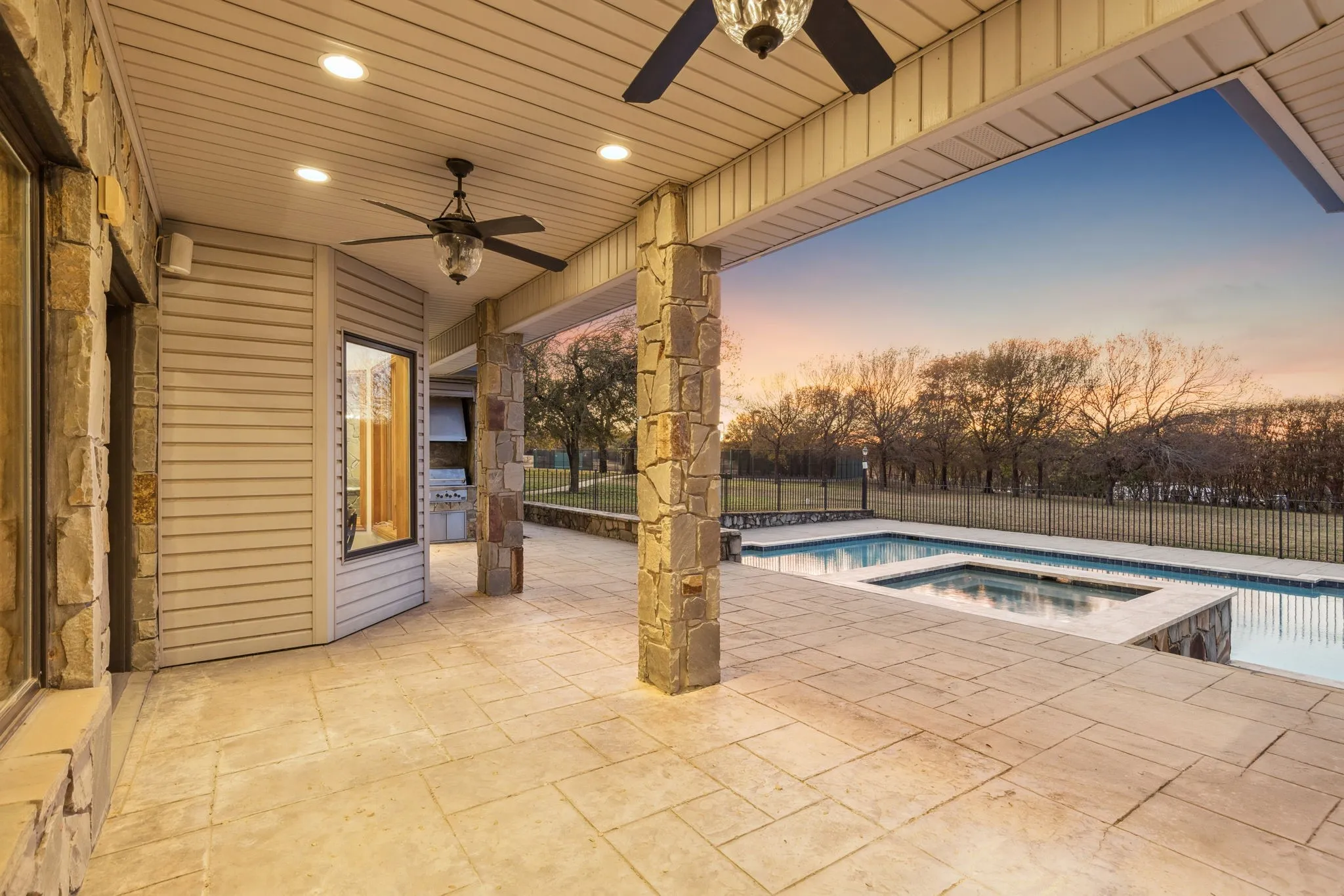 Expansive covered patio featuring stamped concrete flooring, stone columns, and recessed lighting