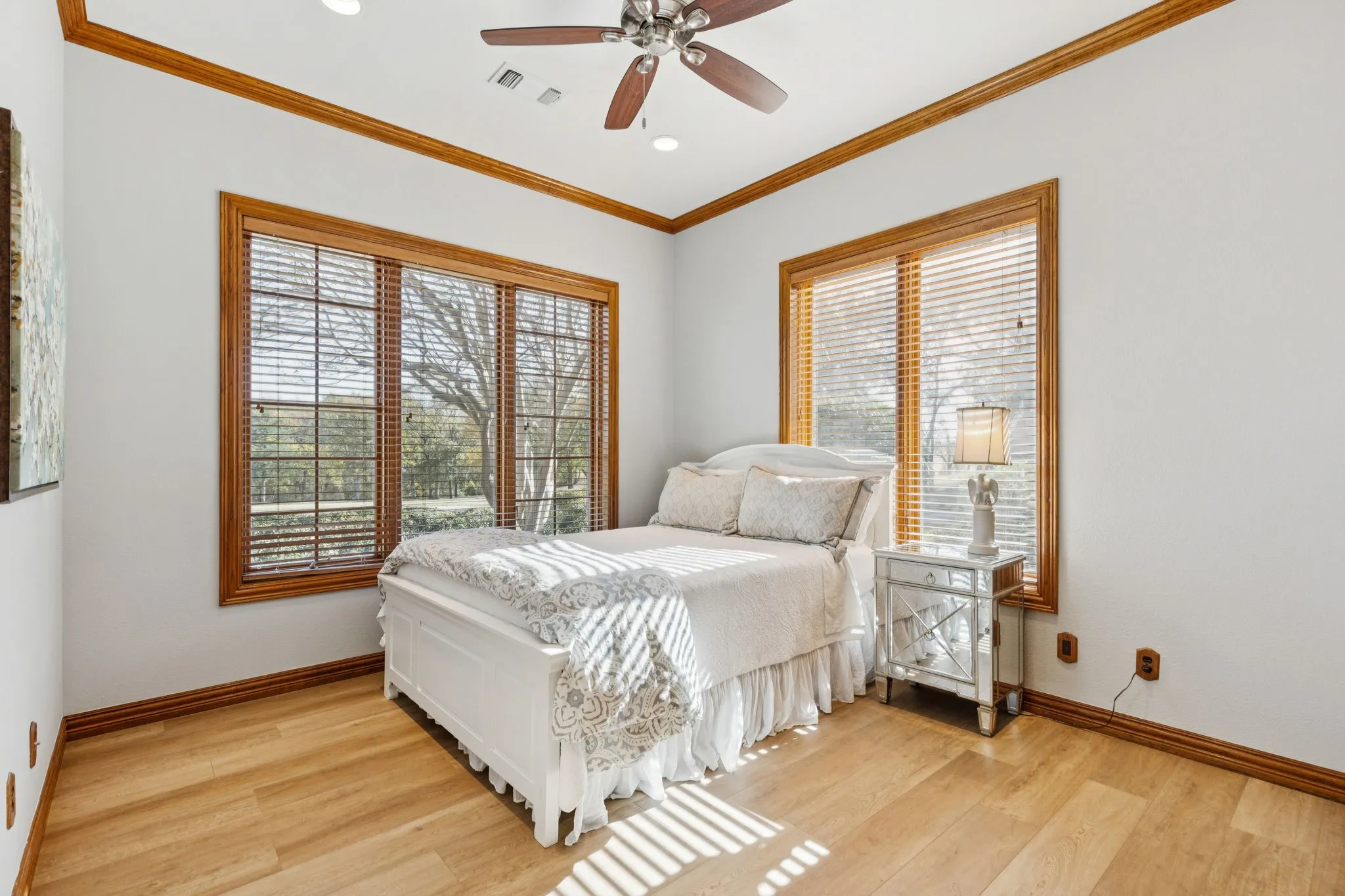 Room featuring light wood-finish flooring, two large windows with wood trim and blinds, a ceiling fan with integrated lighting, and crown molding