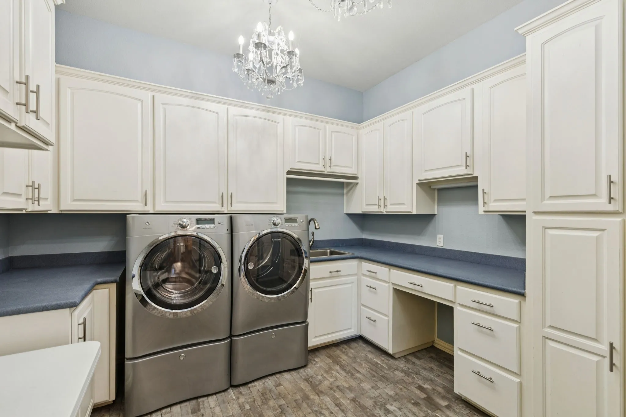 Laundry area featuring extensive white cabinetry, dark countertops, a built-in sink, and wood-finish flooring