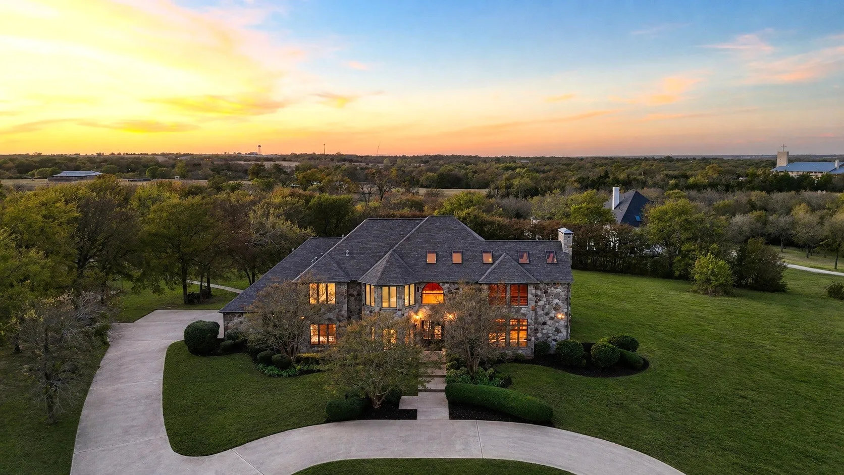 Stone exterior residence featuring a multi-gabled roofline, multiple dormer windows, and a circular driveway