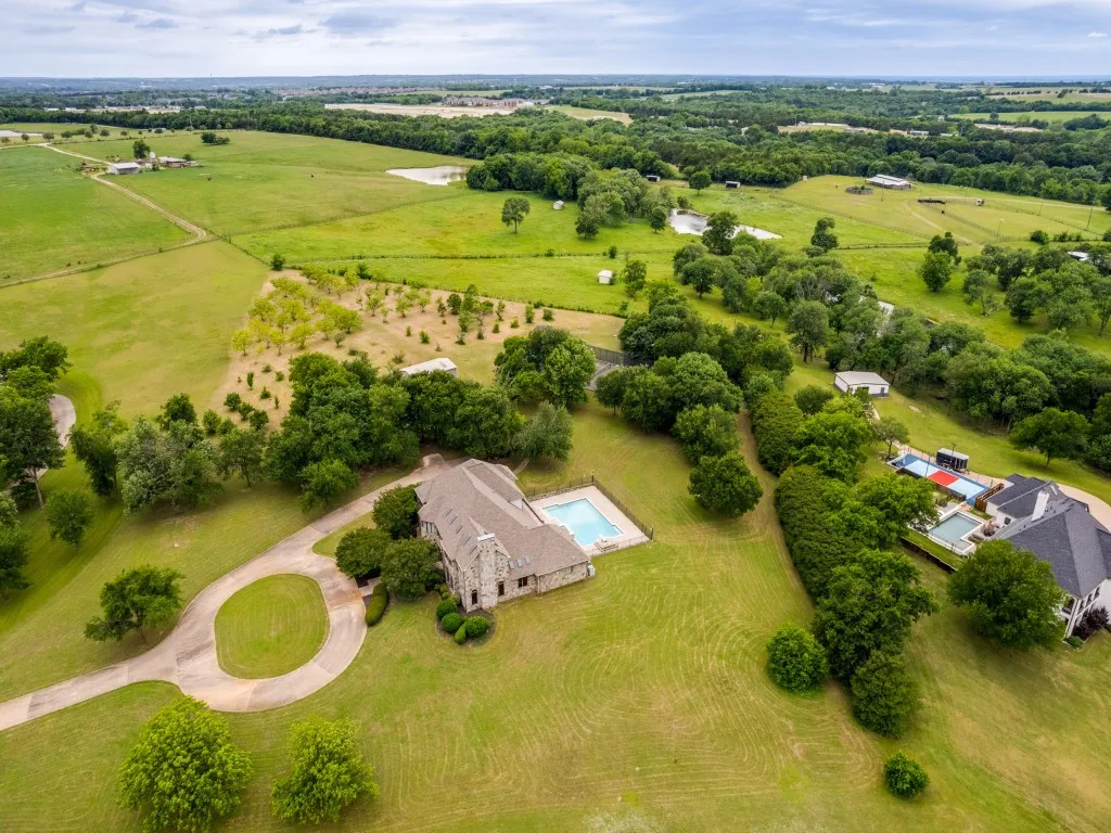 Expansive property featuring a stone exterior residence, a circular driveway, an in-ground swimming pool, and extensive green acreage with mature trees