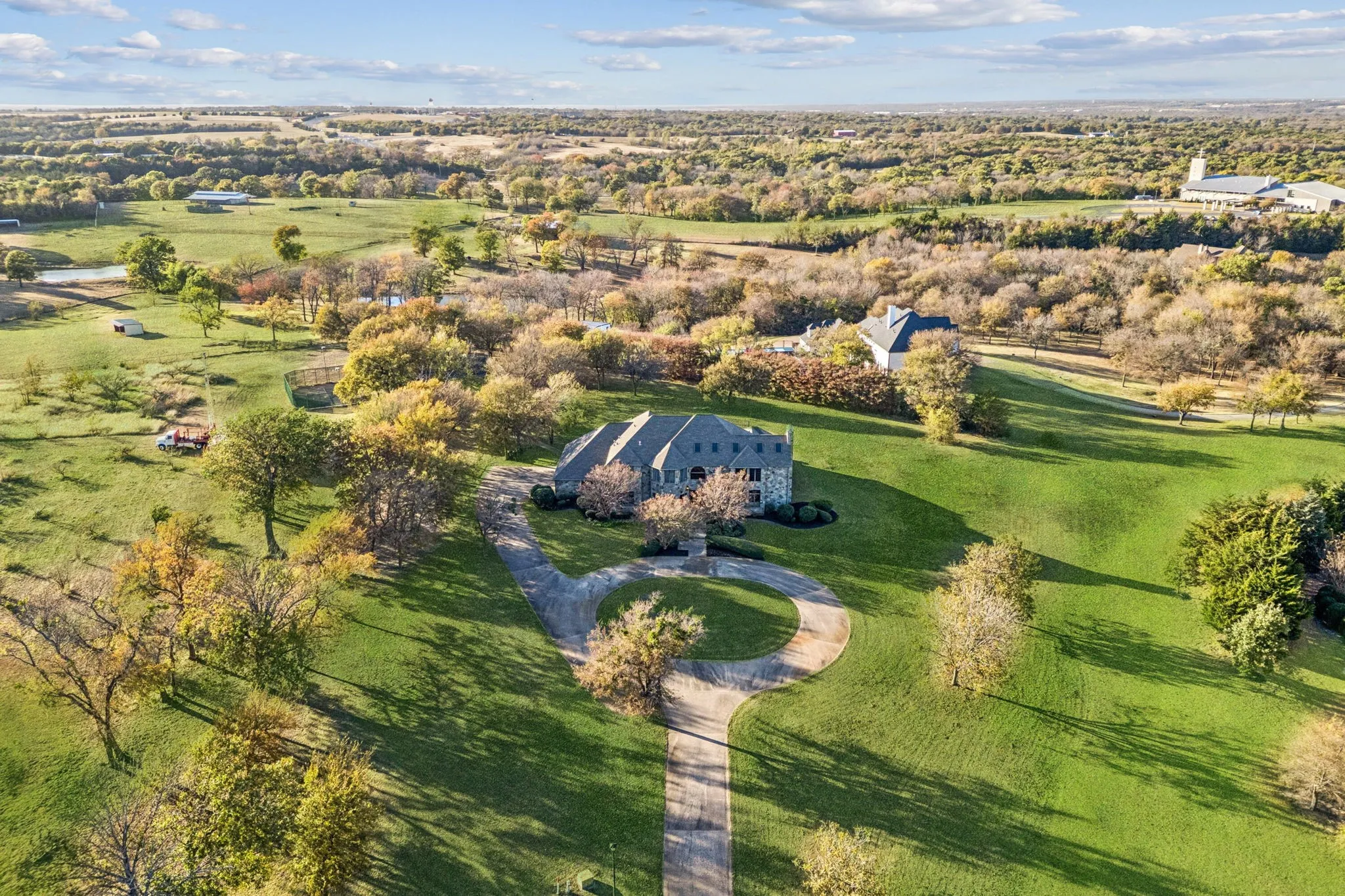 Expansive property featuring a stone and stucco residence with a multi-gabled roofline, set amidst rolling green lawns and mature trees