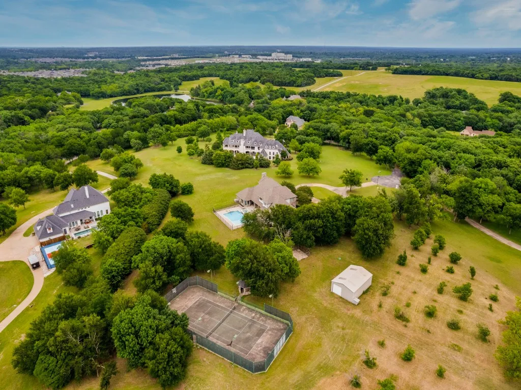 Expansive property featuring multiple structures, a swimming pool with accompanying patio, an outdoor tennis court, and a large detached storage building