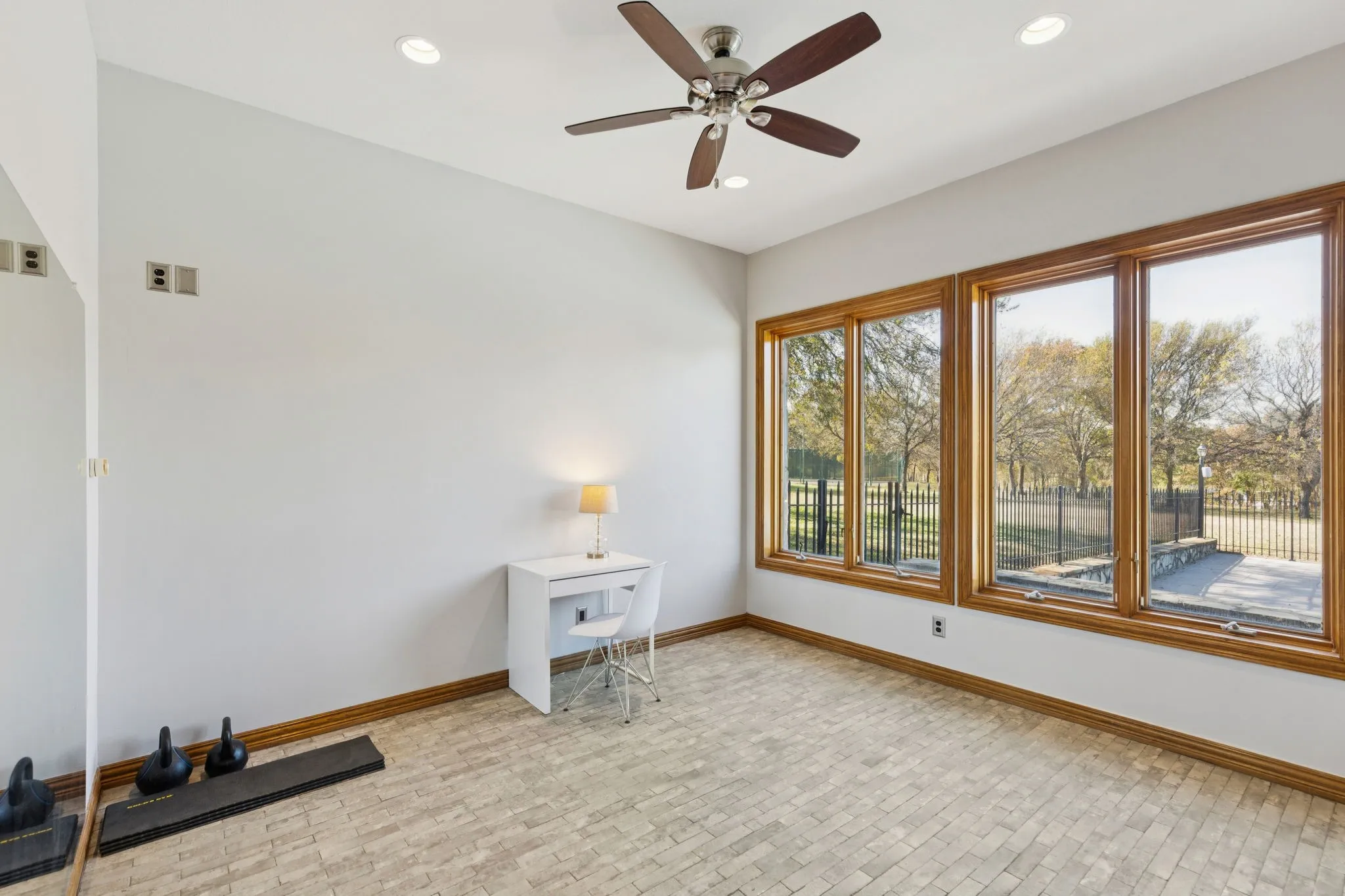 Bright room featuring a ceiling fan with integrated lighting, recessed overhead lights, and a wall of three large windows with wood trim