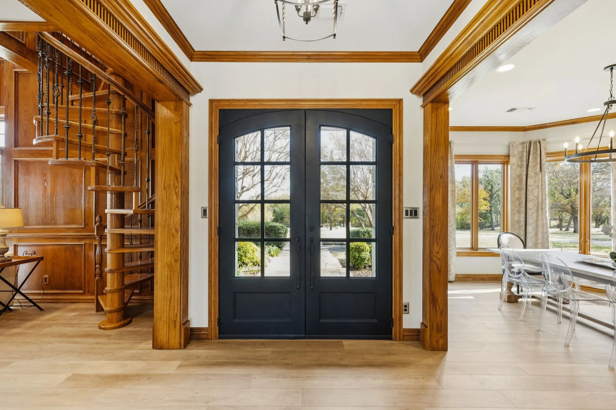 Grand entry featuring double arched doors with divided lites, extensive wood-finish trim, a spiral staircase with wrought iron balusters, and light wood-finish flooring