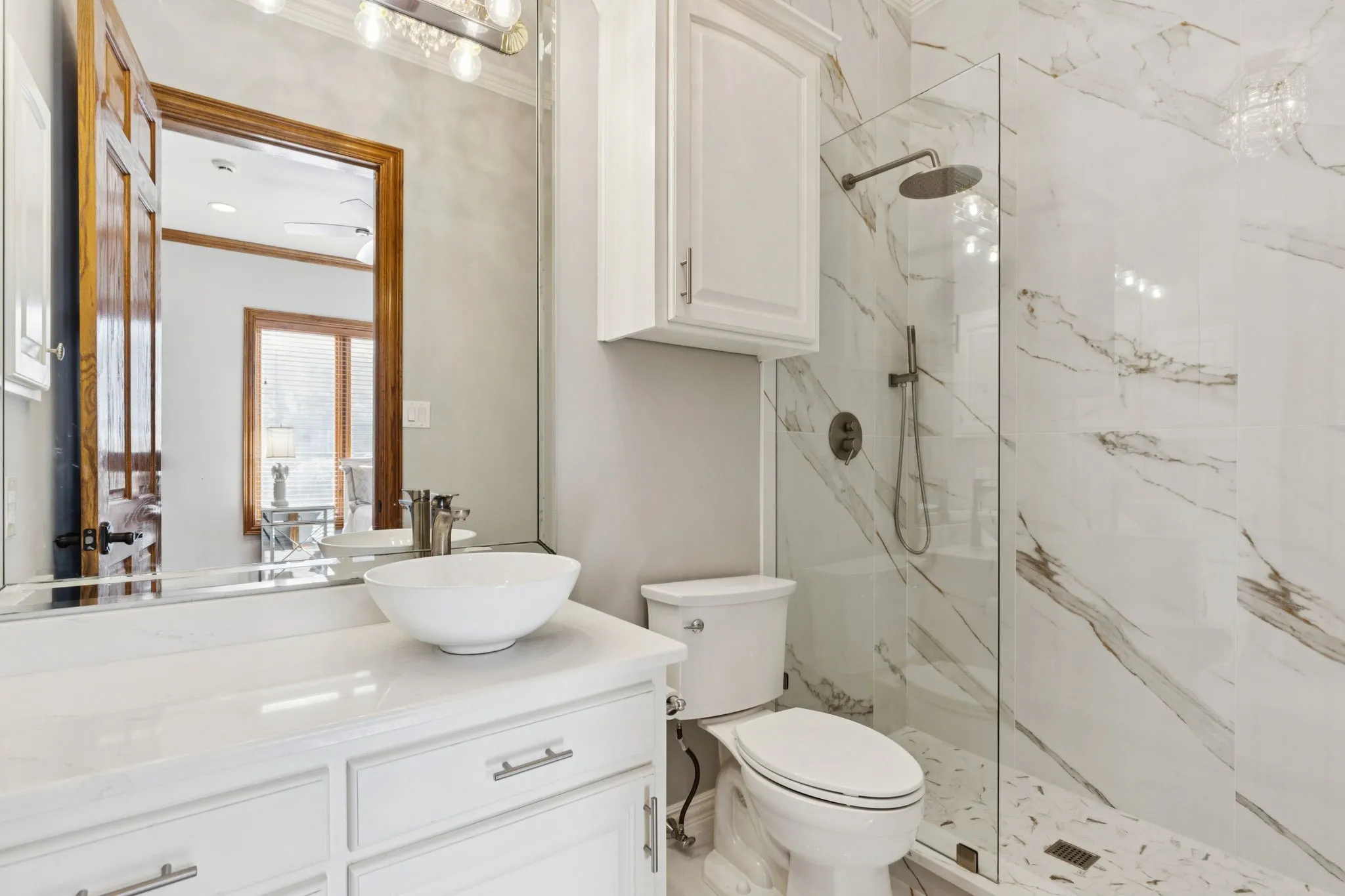 Contemporary bathroom featuring a glass-enclosed shower with a rain shower head, large-format veined tile, and a vessel sink on a white vanity with white cabinetry