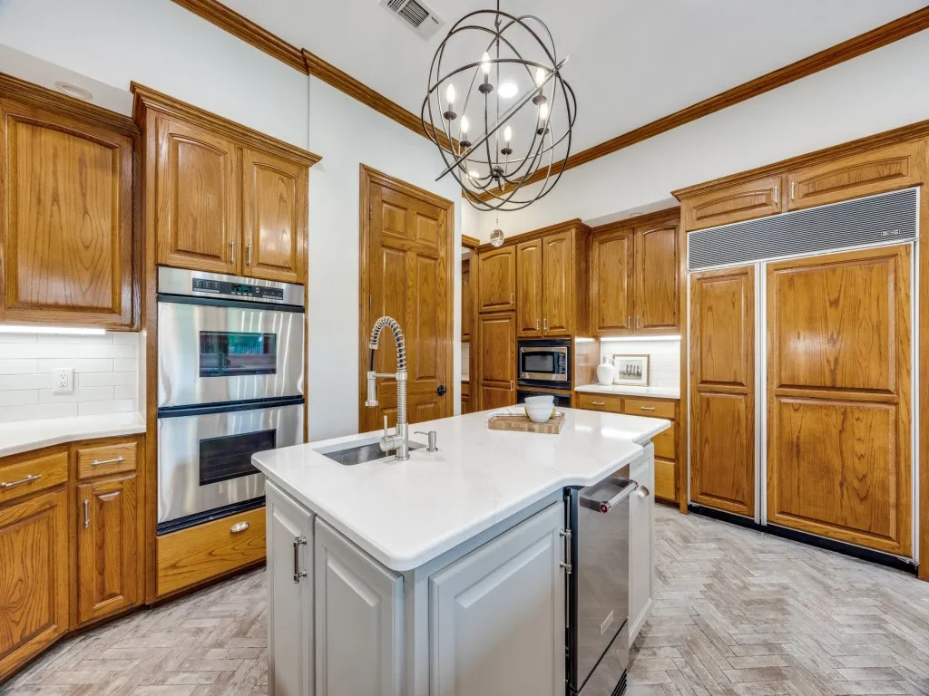 Kitchen featuring a central island with an undermount sink and a stainless steel dishwasher, along with a double oven, built-in microwave, and integrated refrigerator