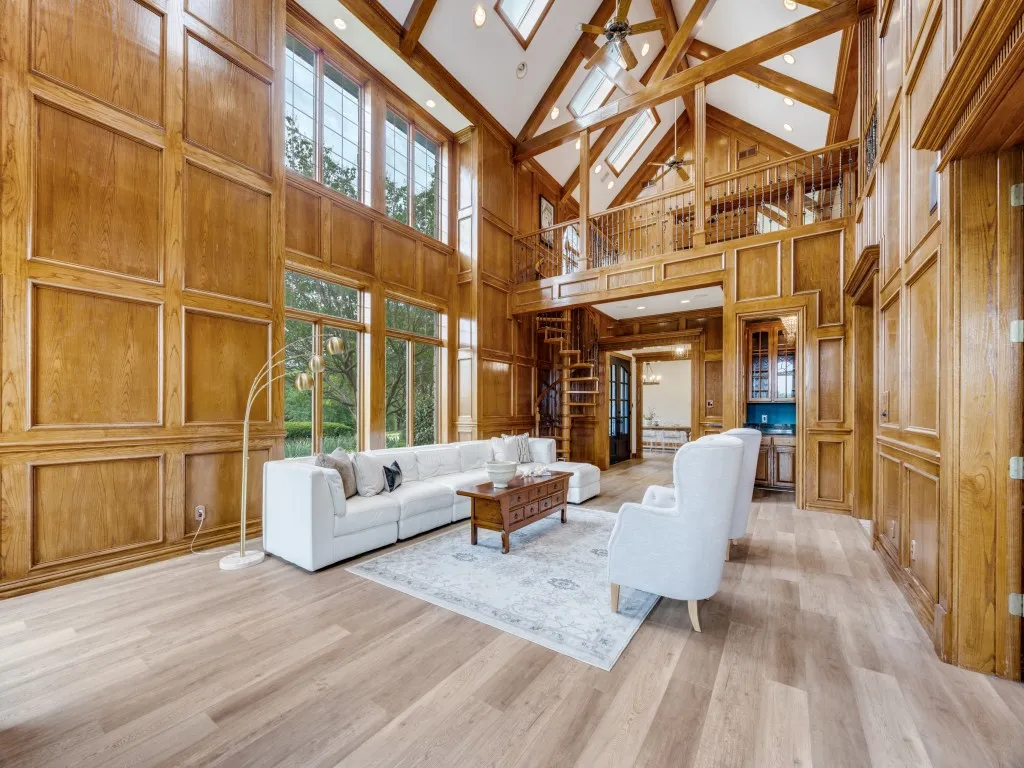 Grand living area featuring soaring ceilings with exposed wood beams, expansive paneling, and a floor-to-ceiling window wall