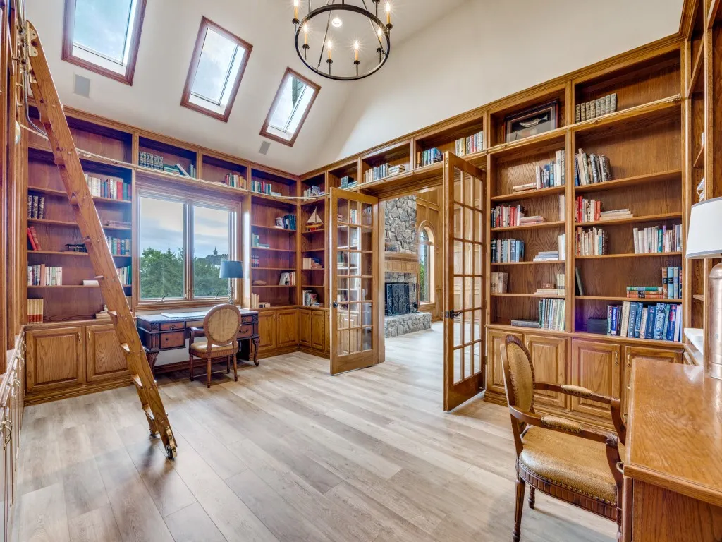 Vaulted ceiling study featuring extensive built-in oak shelving, a rolling ladder, and skylights