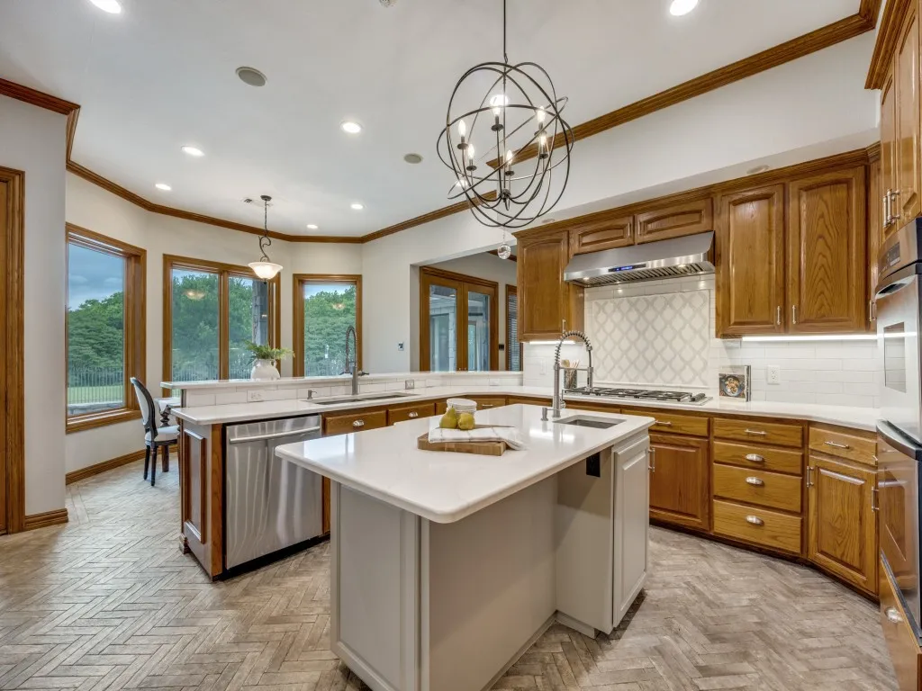 Kitchen featuring light wood-finish herringbone flooring, wood cabinetry, stainless steel appliances, a center island with a white countertop, and a bay window area