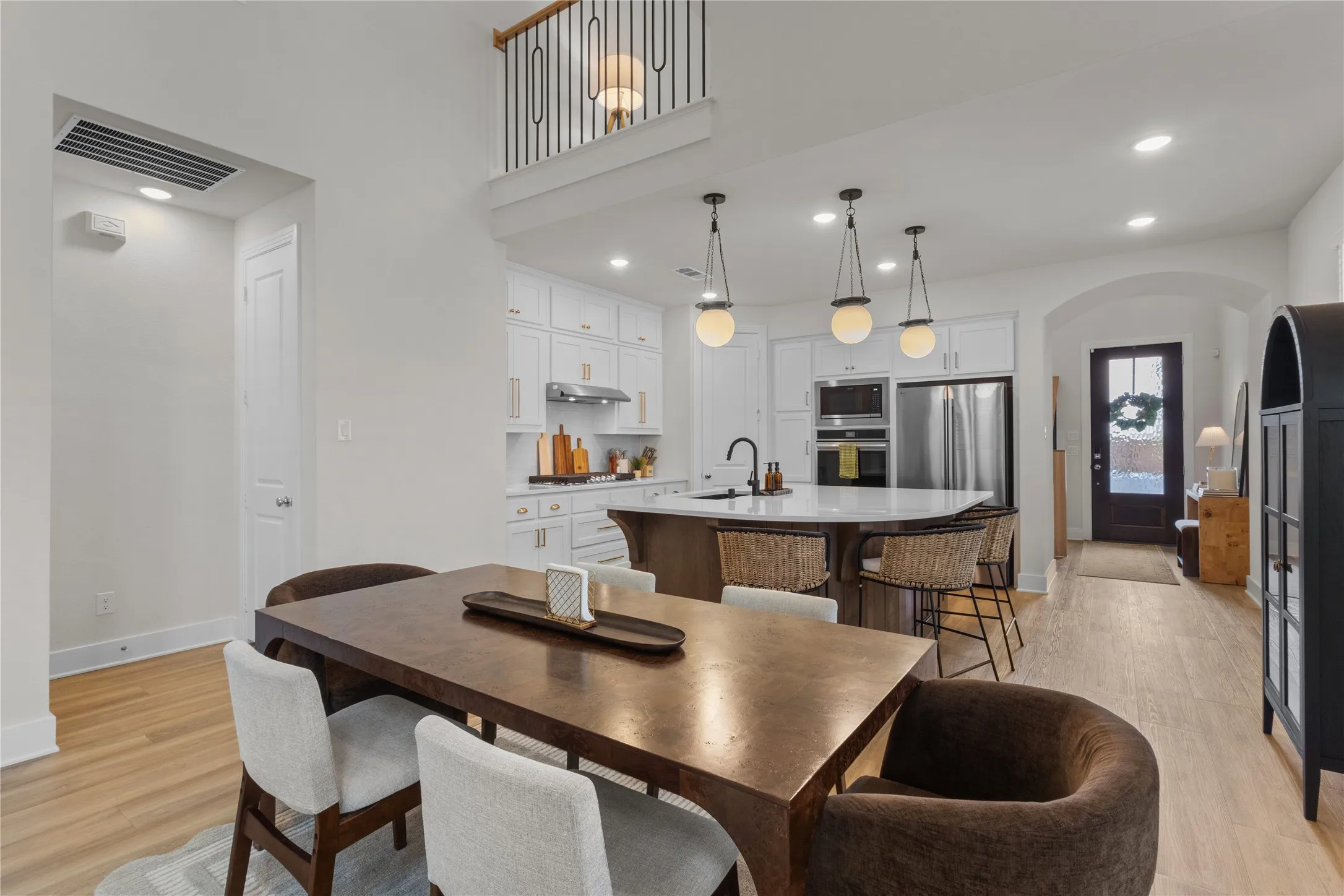 Open-concept living area featuring light wood-finish flooring, a two-story ceiling, and a kitchen with an island, pendant lighting, and stainless steel appliances