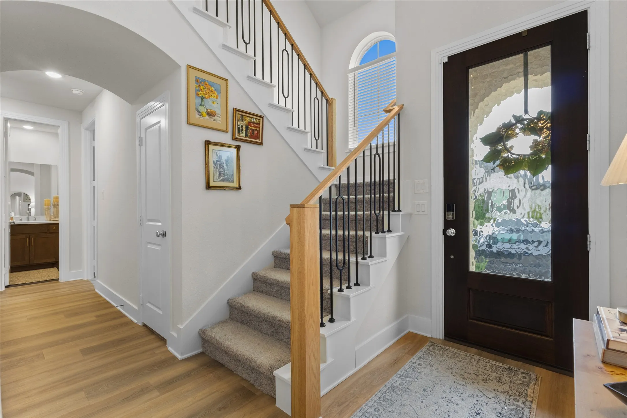 Entry foyer with wood-finish flooring, a dark wood-finish door with decorative glass, and an arched transom window