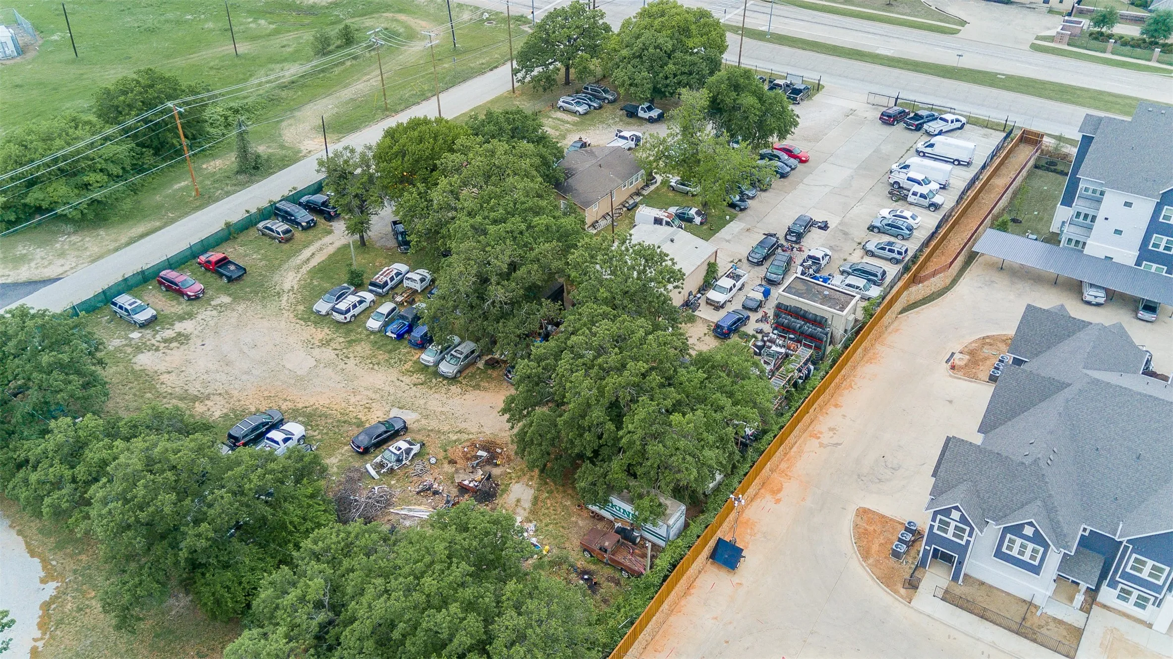 Expansive commercial property featuring a paved parking area, a central building, perimeter fencing, and mature trees
