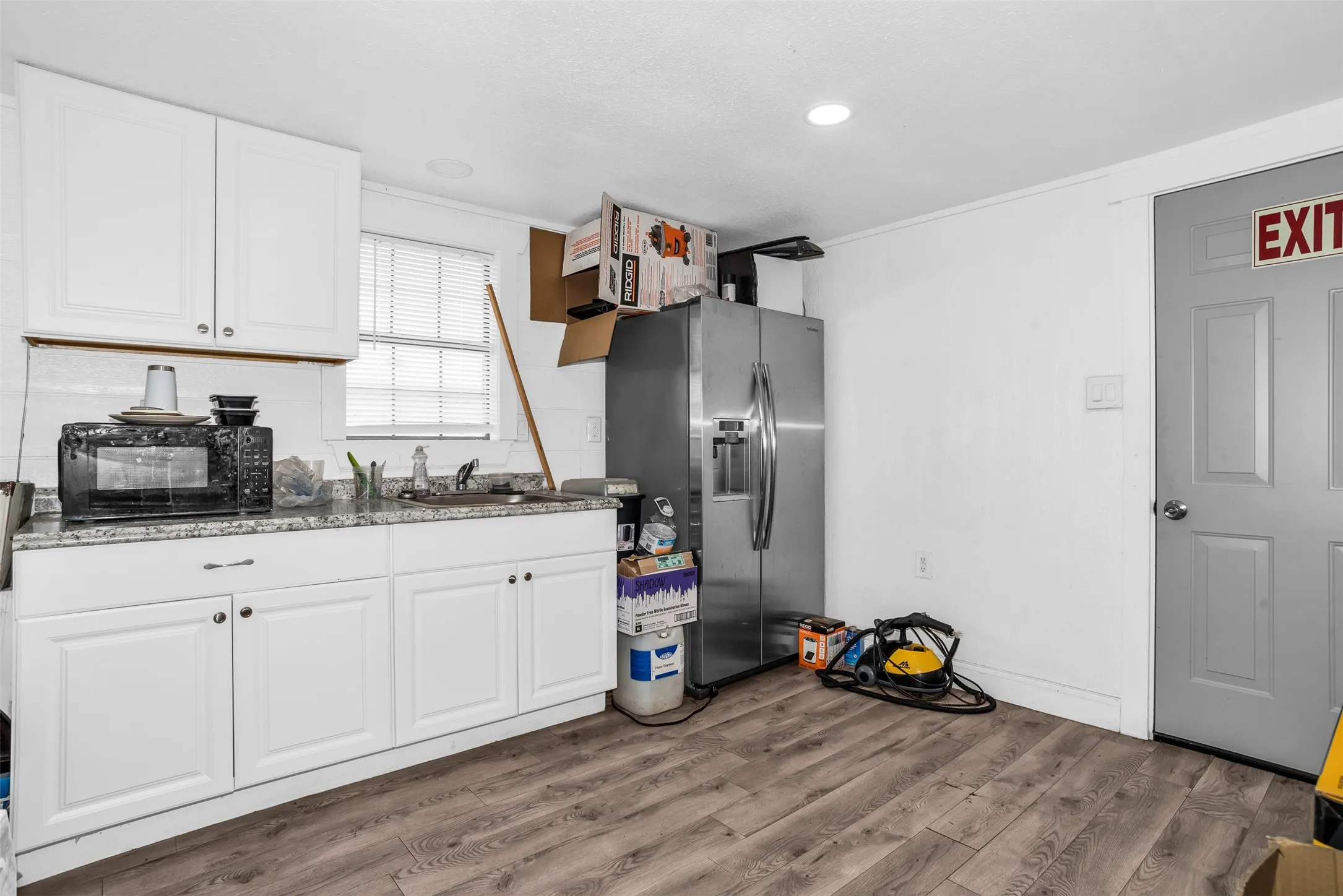 Kitchenette area featuring wood-finish flooring, white cabinetry, and a granite-style countertop