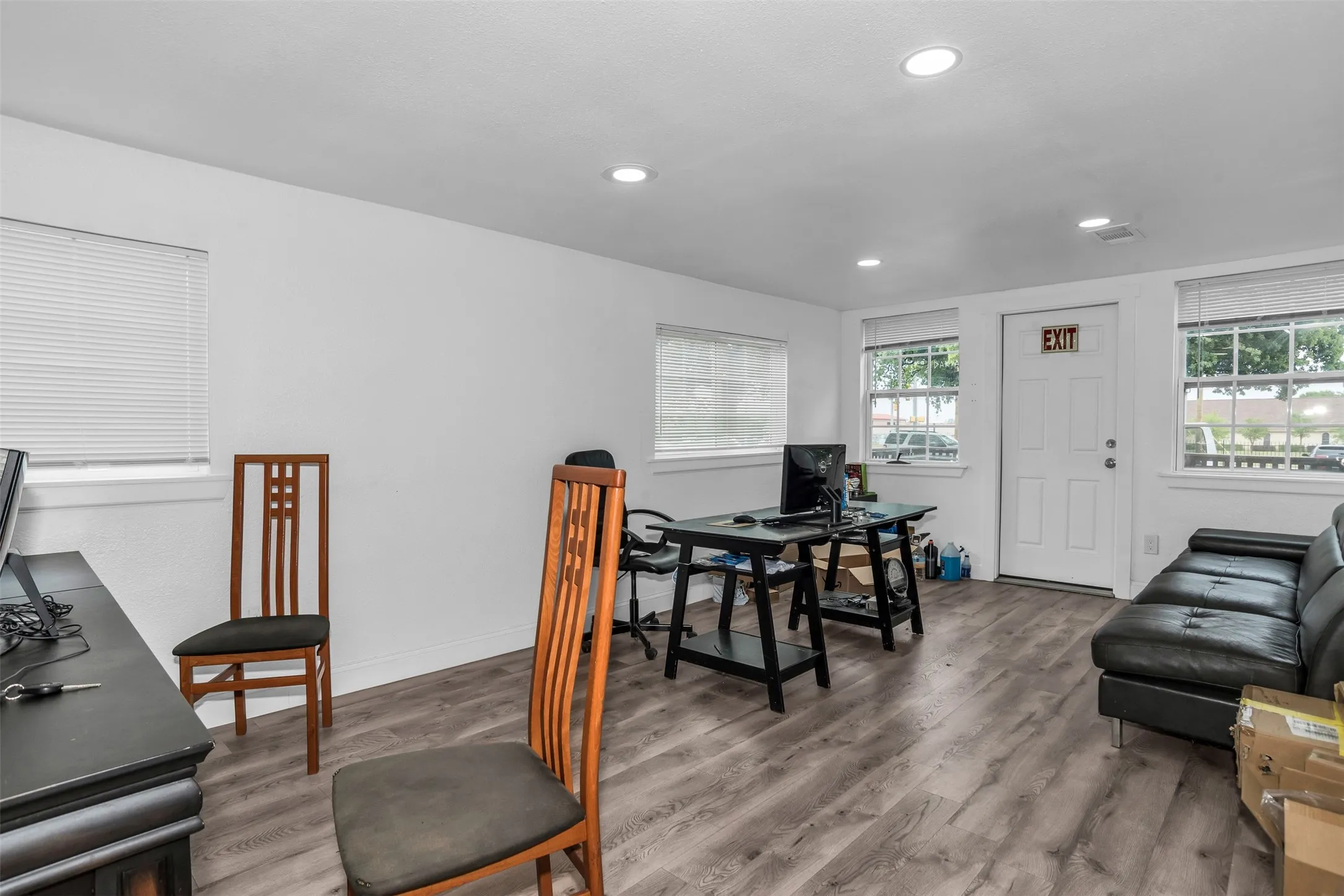 Spacious room featuring light wood-finish flooring and multiple windows with blinds