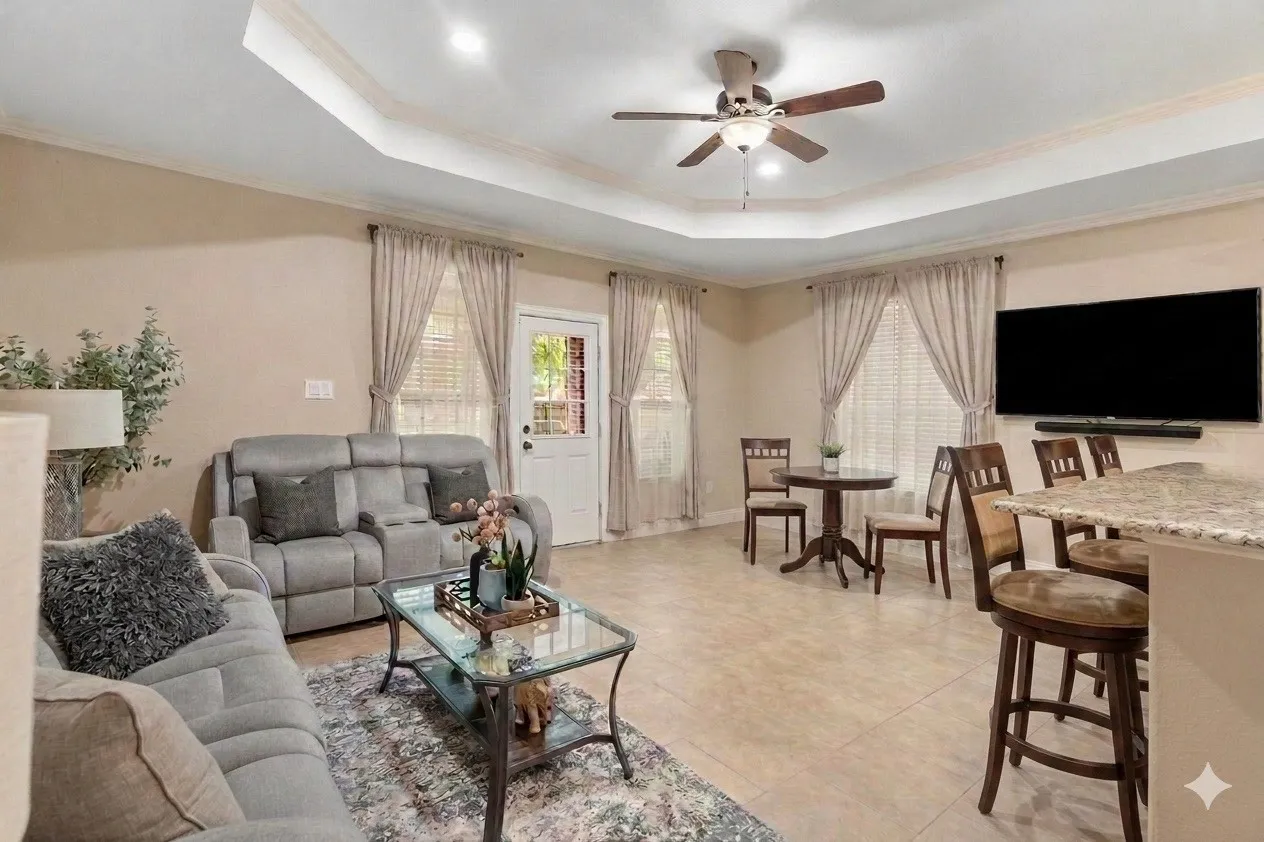 Spacious living area featuring a tray ceiling, ceiling fan, recessed lighting, tile flooring, and multiple windows