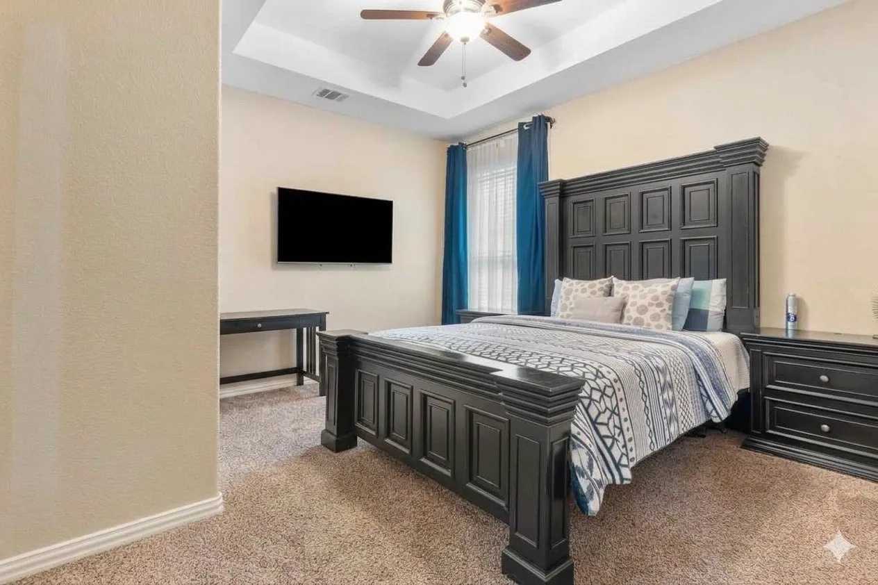 Tray ceiling with a ceiling fan, wall-mounted television, and neutral carpeting