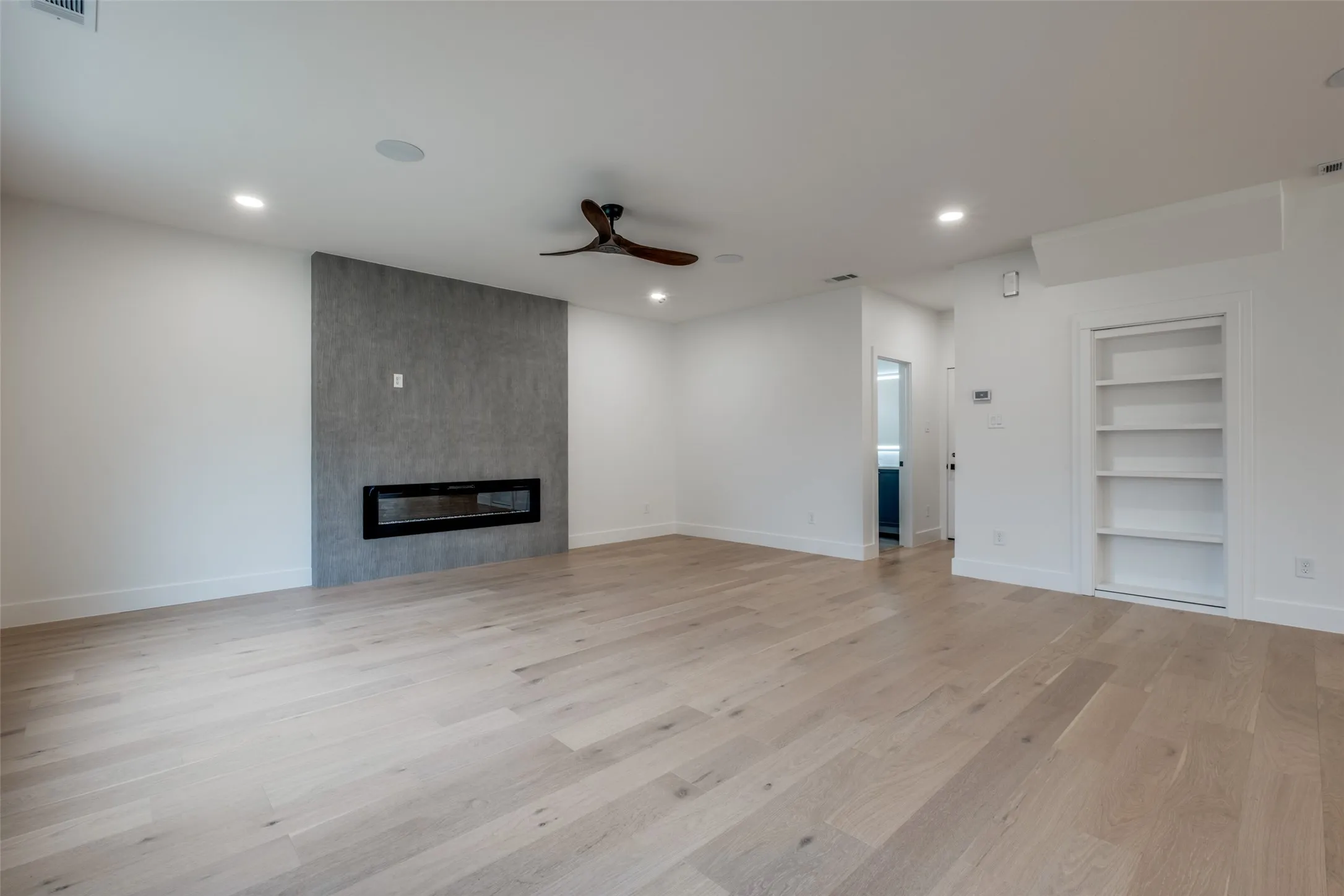 Living room with built in shelves, light wood-style floors, ceiling fan, recessed lighting, and a large fireplace