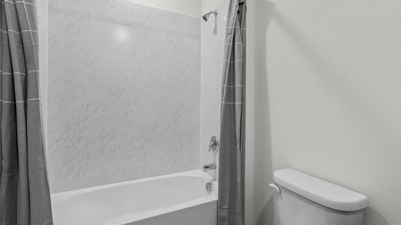Bathtub and shower combination featuring a white tub, light-colored shower surround, and chrome fixtures